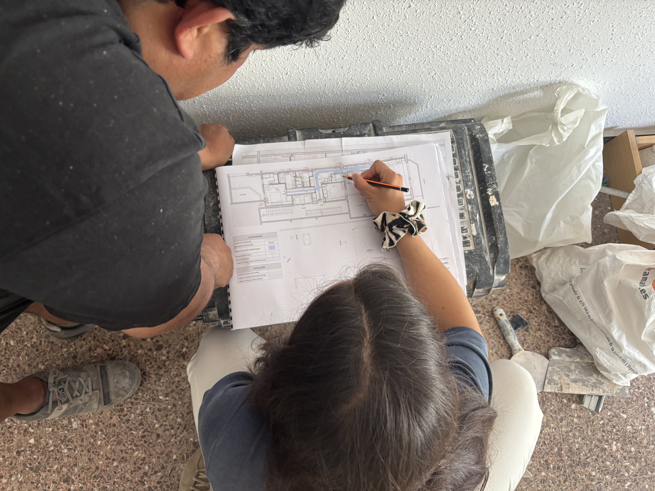 Vista cenital de dos personas revisando y realizando anotaciones sobre planos arquitectónicos en una obra
