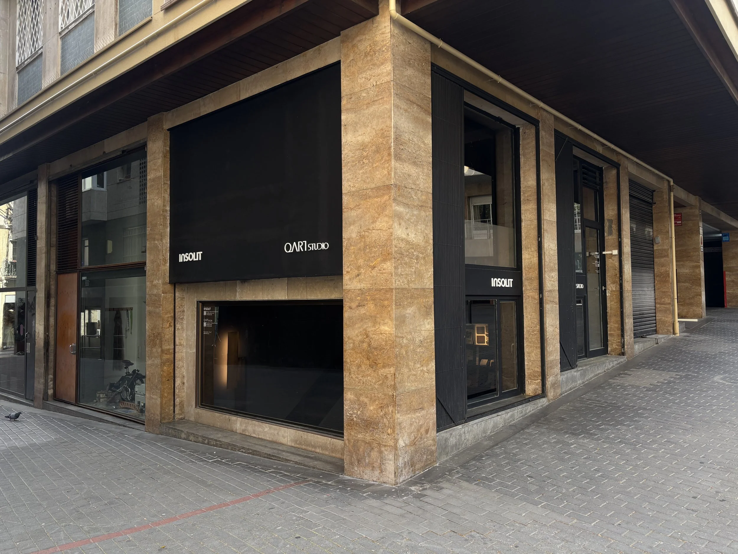 Vista exterior de un edificio comercial con ventanas y storefronts en un entorno urbano, con aceras de pavimento y un logotipo visible que dice 'INSOLIT' y 'OAR1 STUDIO'.