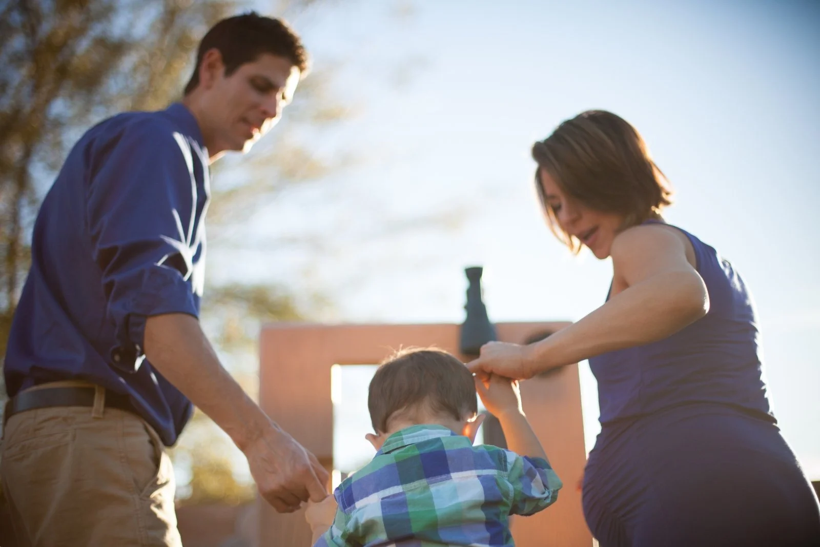 dad, mom, and little boy play on the slide. Mom is pregnant. Photographed during a Carlsbad family photography session.