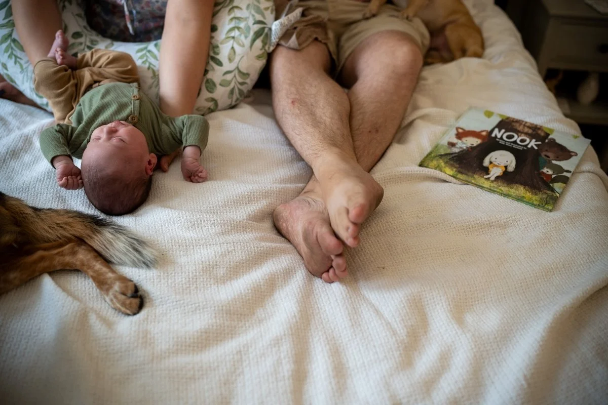 newborn baby, dad's feet, and dog's paw all lay on the bed during a Tucson newborn photography session.