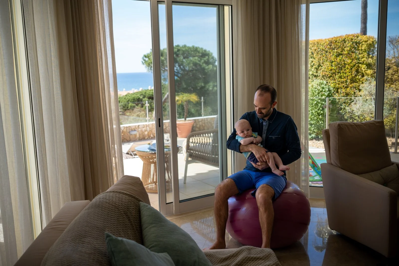 Dad rocks baby to sleep on bouncy ball in living room.