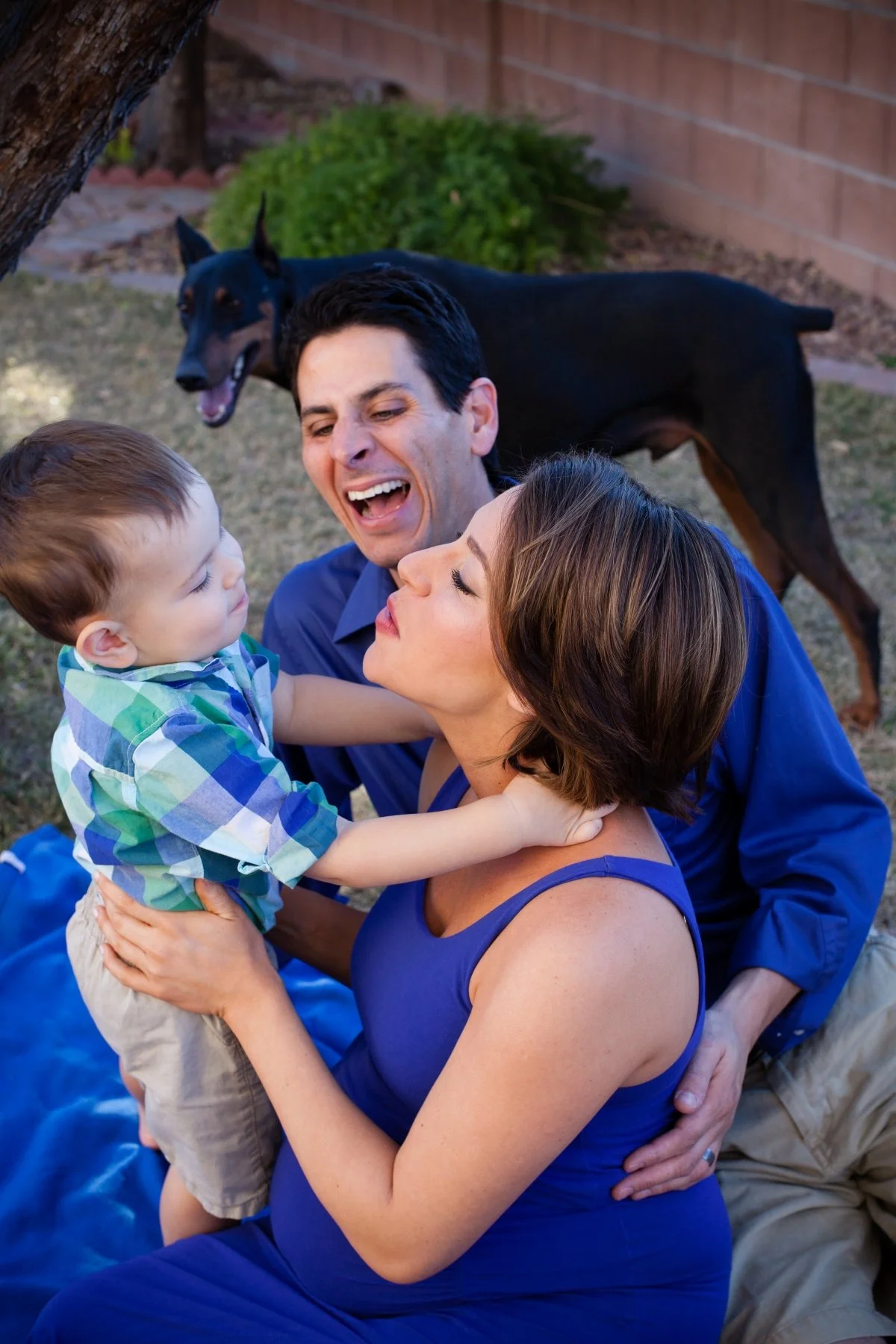 woman, man, and child sit on the grass with black dog during a Carlsbad maternity family photography session.
