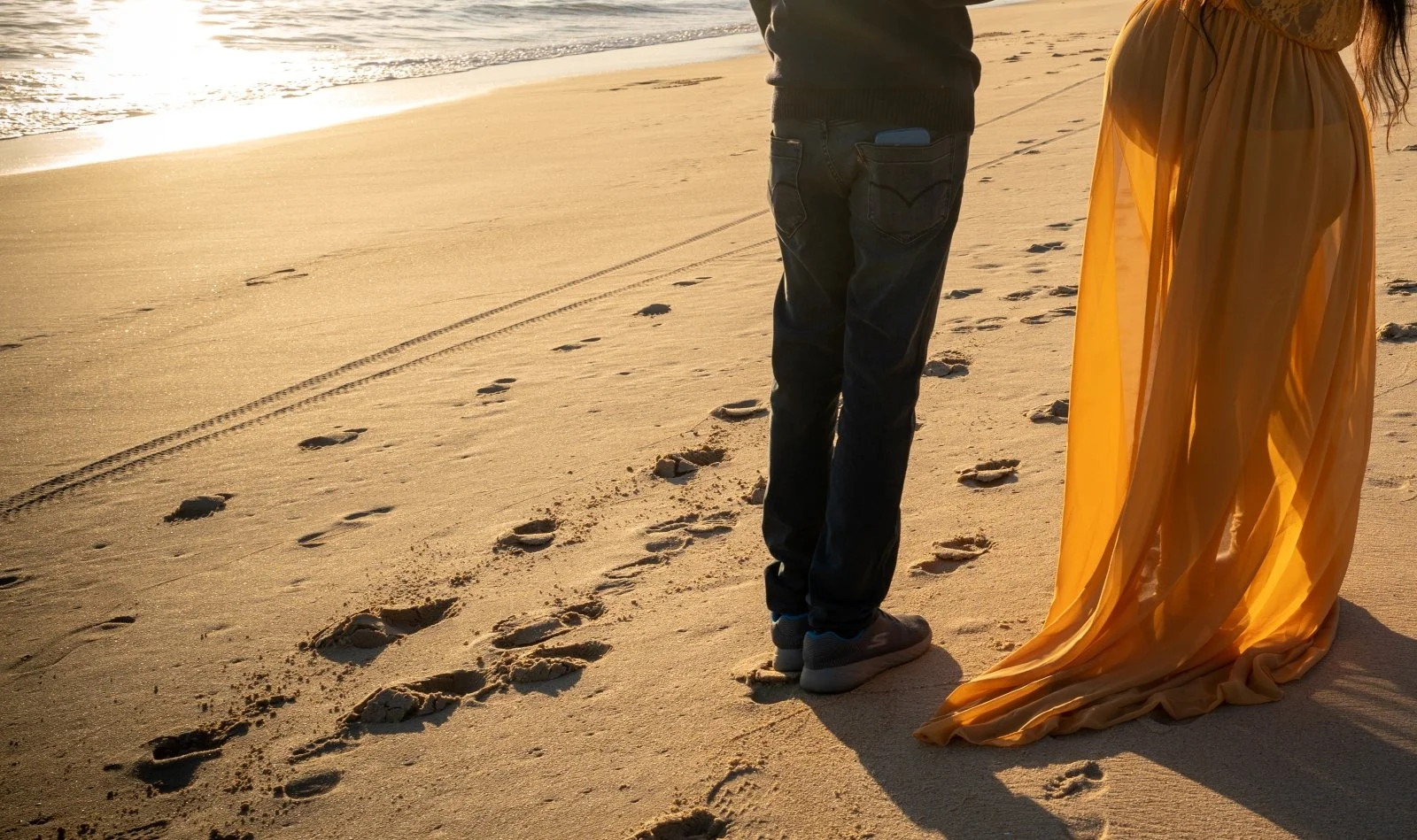 woman in orange dress with man in black during a Carlsbad maternity session