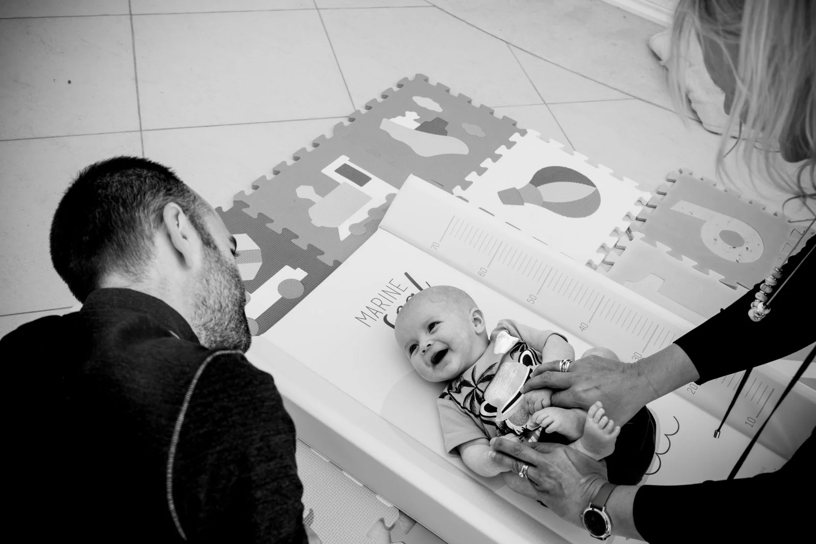 Mom and Dad change baby's diaper on a floor mat.