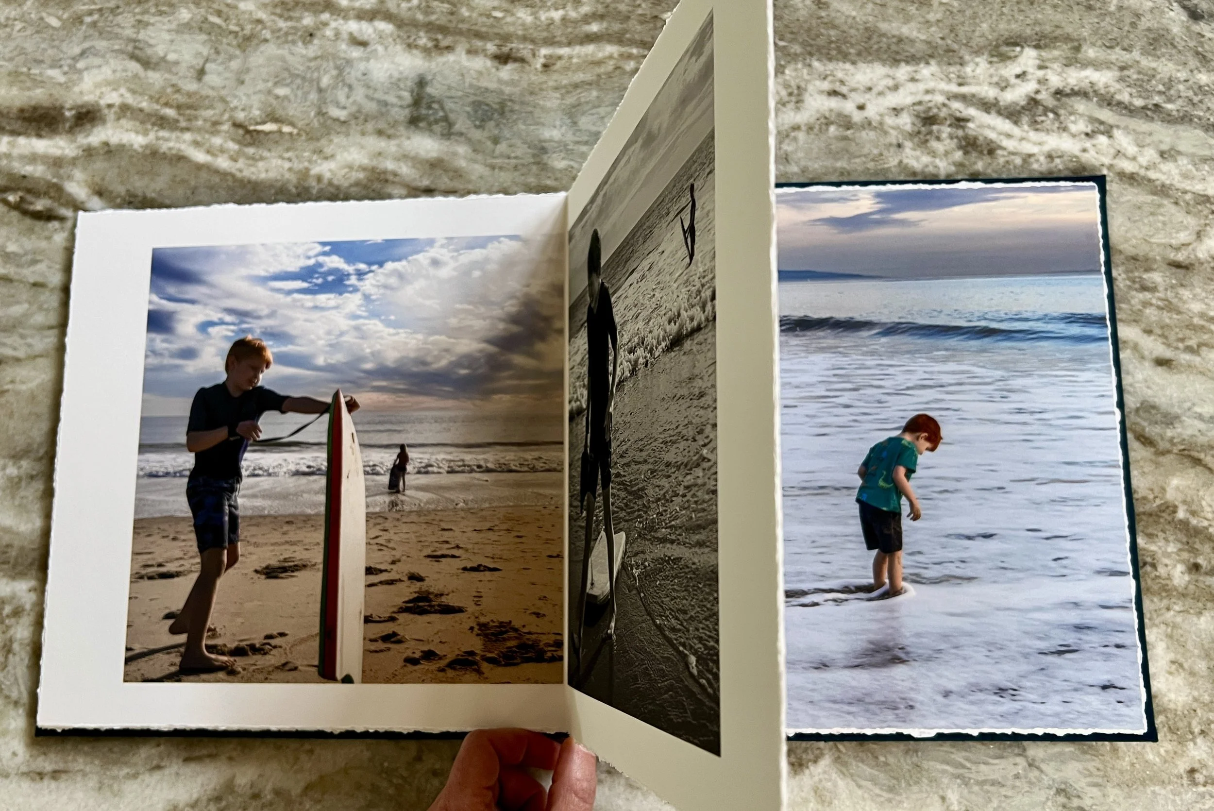 Open photo album displaying three photos of children at the beach. The first is a boy carrying a surfboard, the second is a boy standing in the water, and the third is a boy walking in the tide by Tucson family photographer Michelle Molnar.
