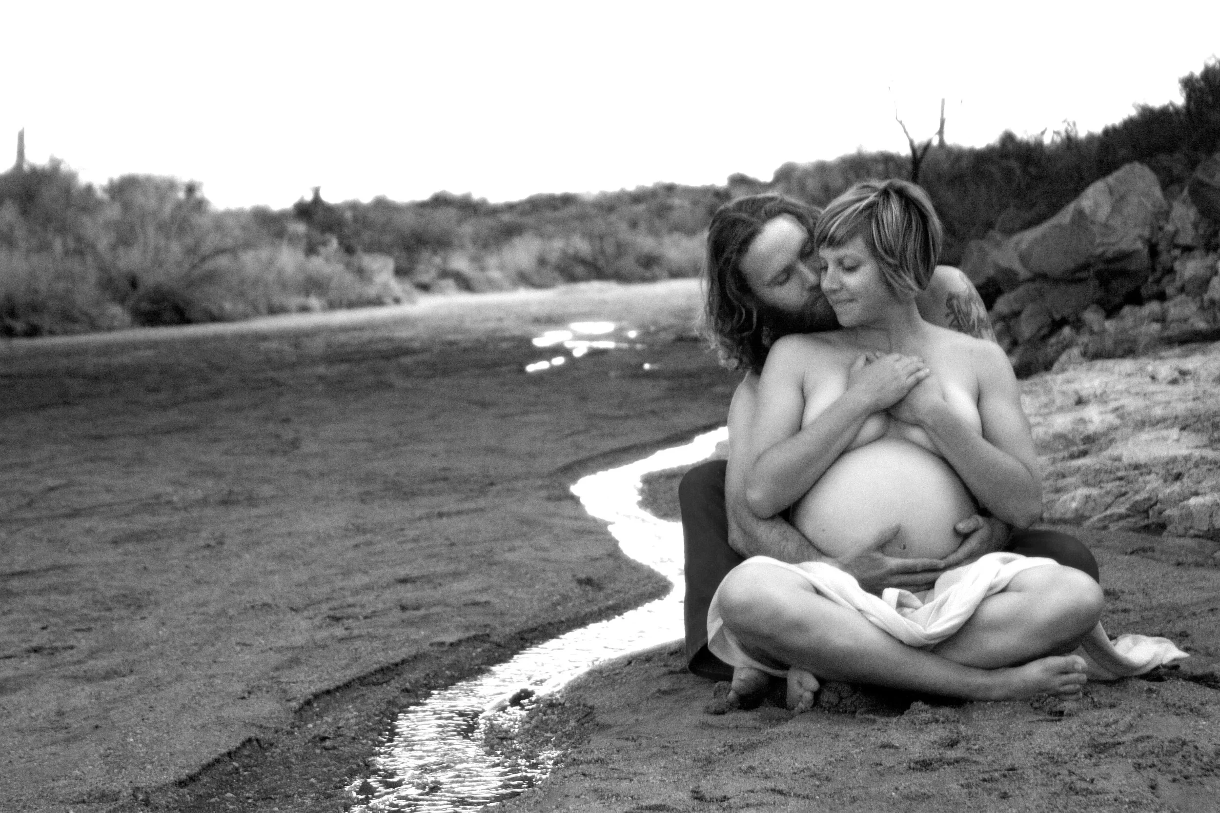 man and pregnant woman sit on the sand during a pregnancy photography session in Carlsbad.