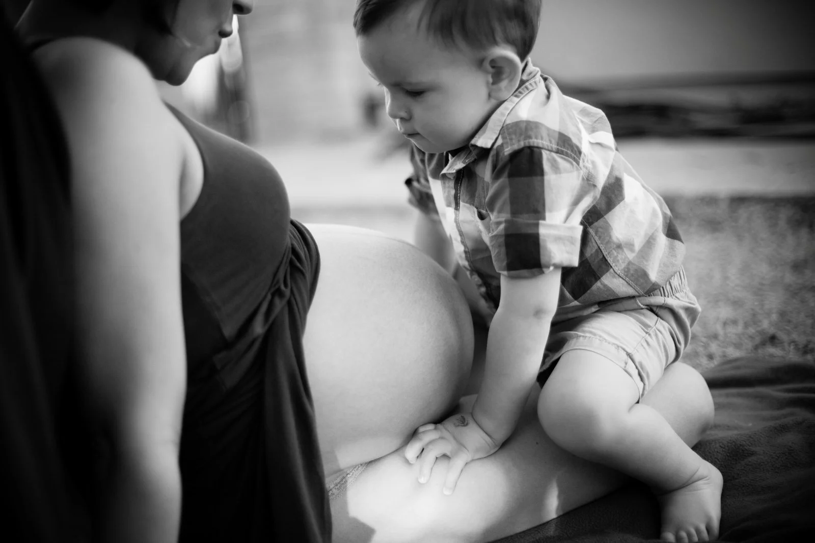 young boy sits on pregnant mom's lap in a black and white maternity session in San Diego