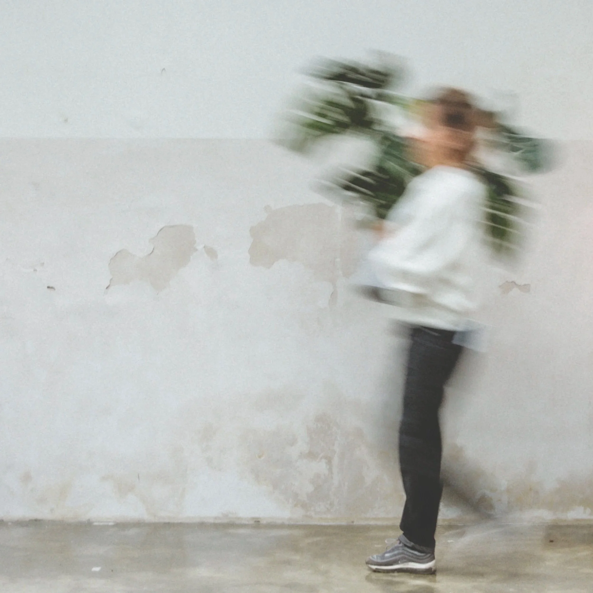 Verschwommene Person mit Rucksack gegen eine beschädigte weiße Wand