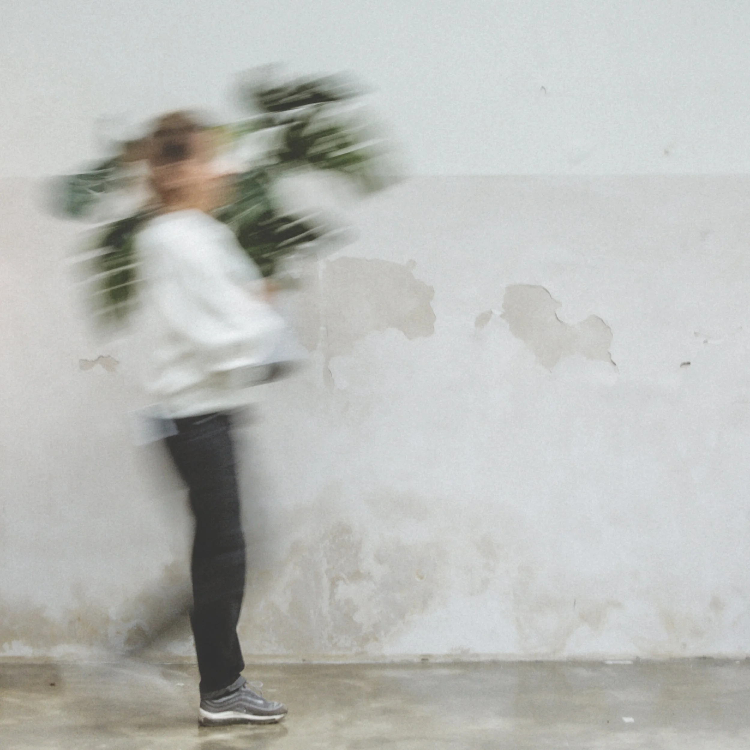 Verwirbeltes Foto eines Menschen mit Rucksack, der vor einer Wand steht, die tapetenartig beschädigt ist.