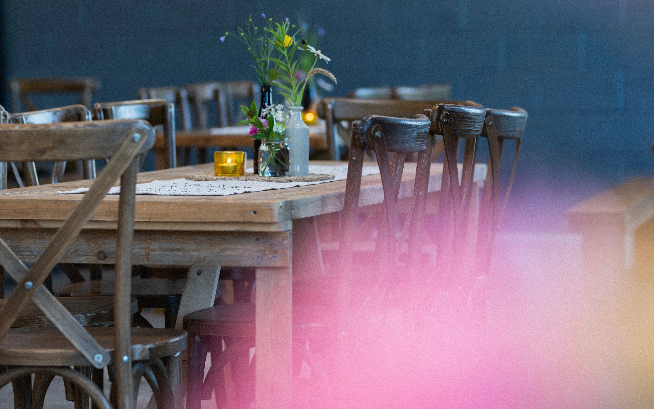 Rustic dining table with wooden chairs, decorated with a vase of wildflowers and a lit yellow candle.