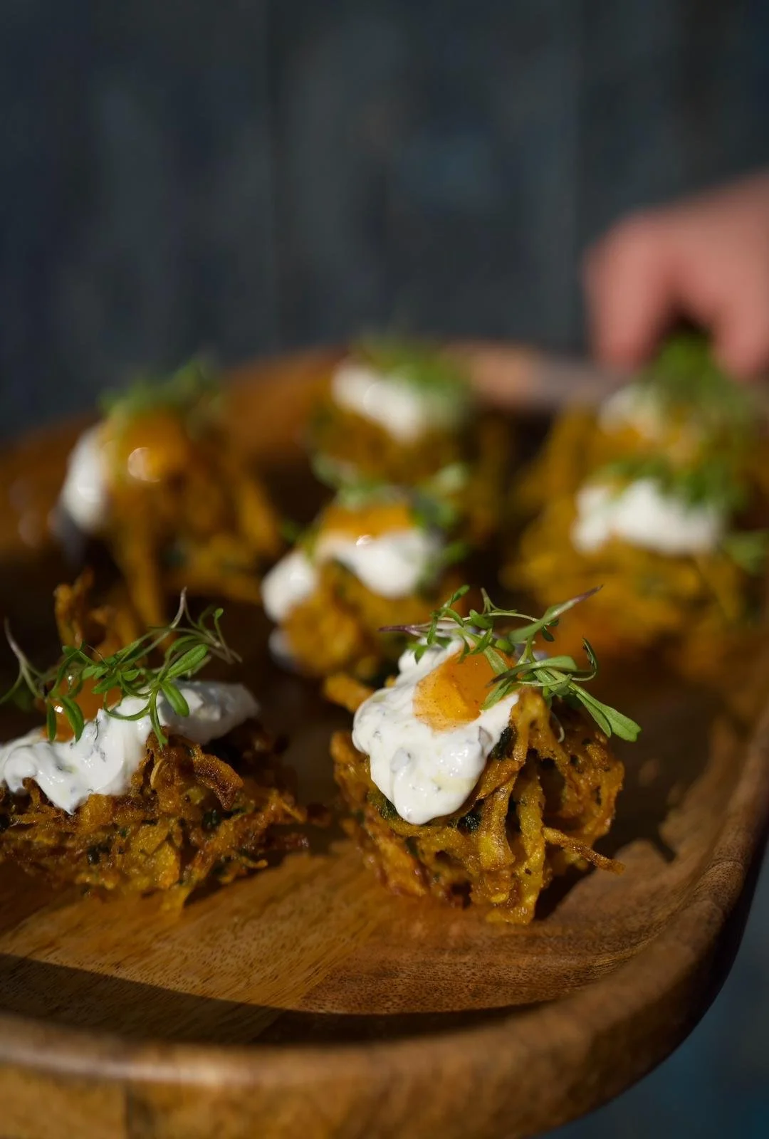 Close-up of several crispy fritters topped with dollops of white sauce and garnished with green herbs on a wooden platter.