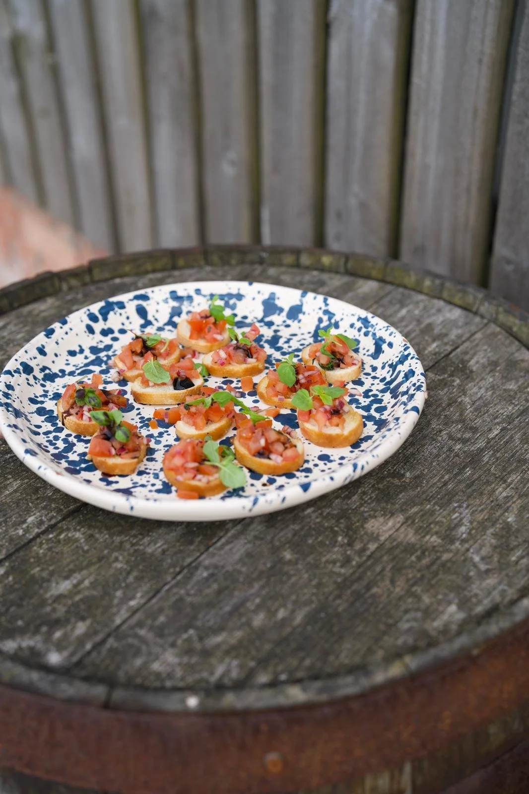 Plate with small bruschetta topped with tomatoes and herbs on a wooden surface.