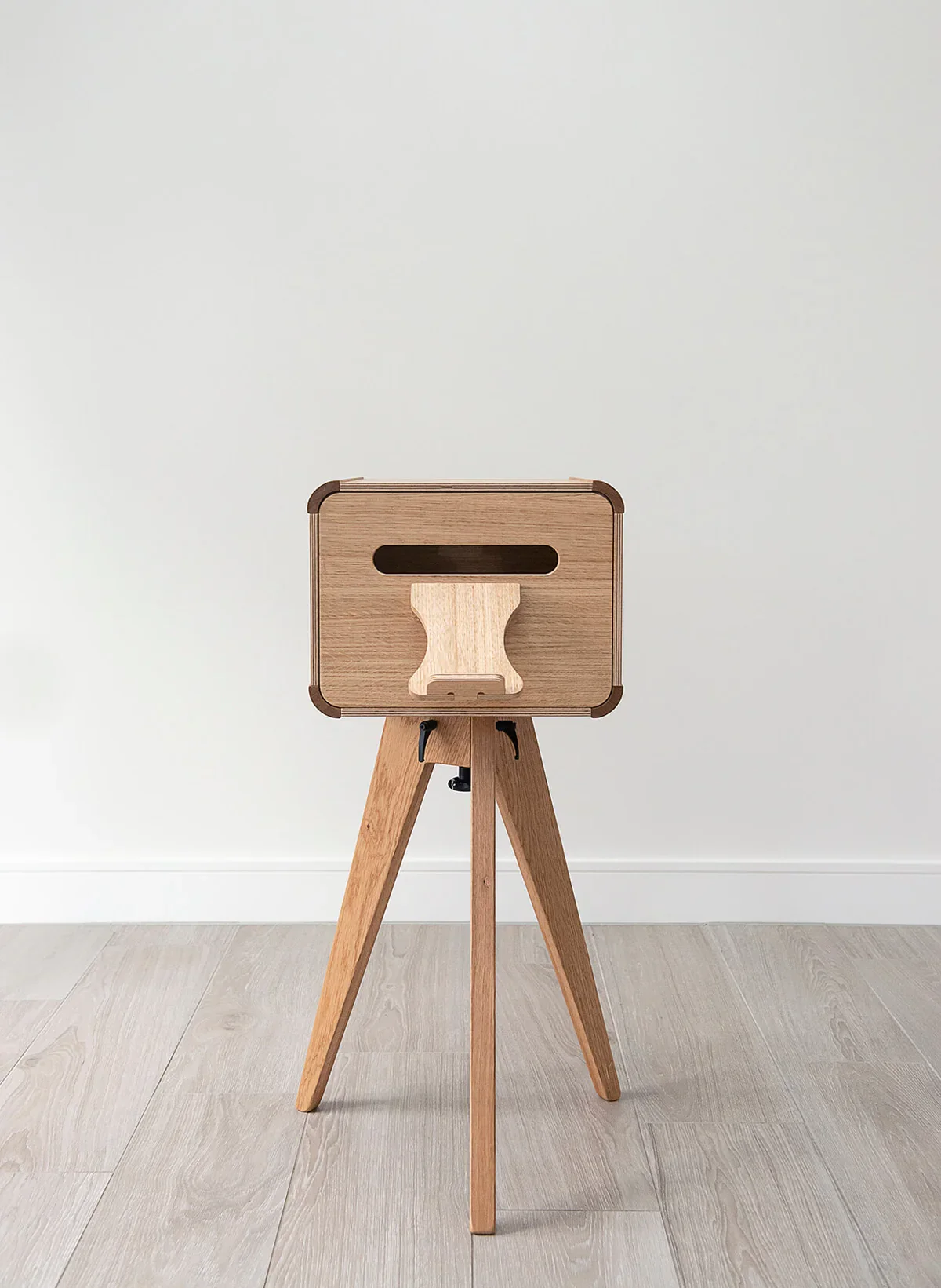 A wooden high chair with a modern design, placed against a white wall and on a light wood floor.