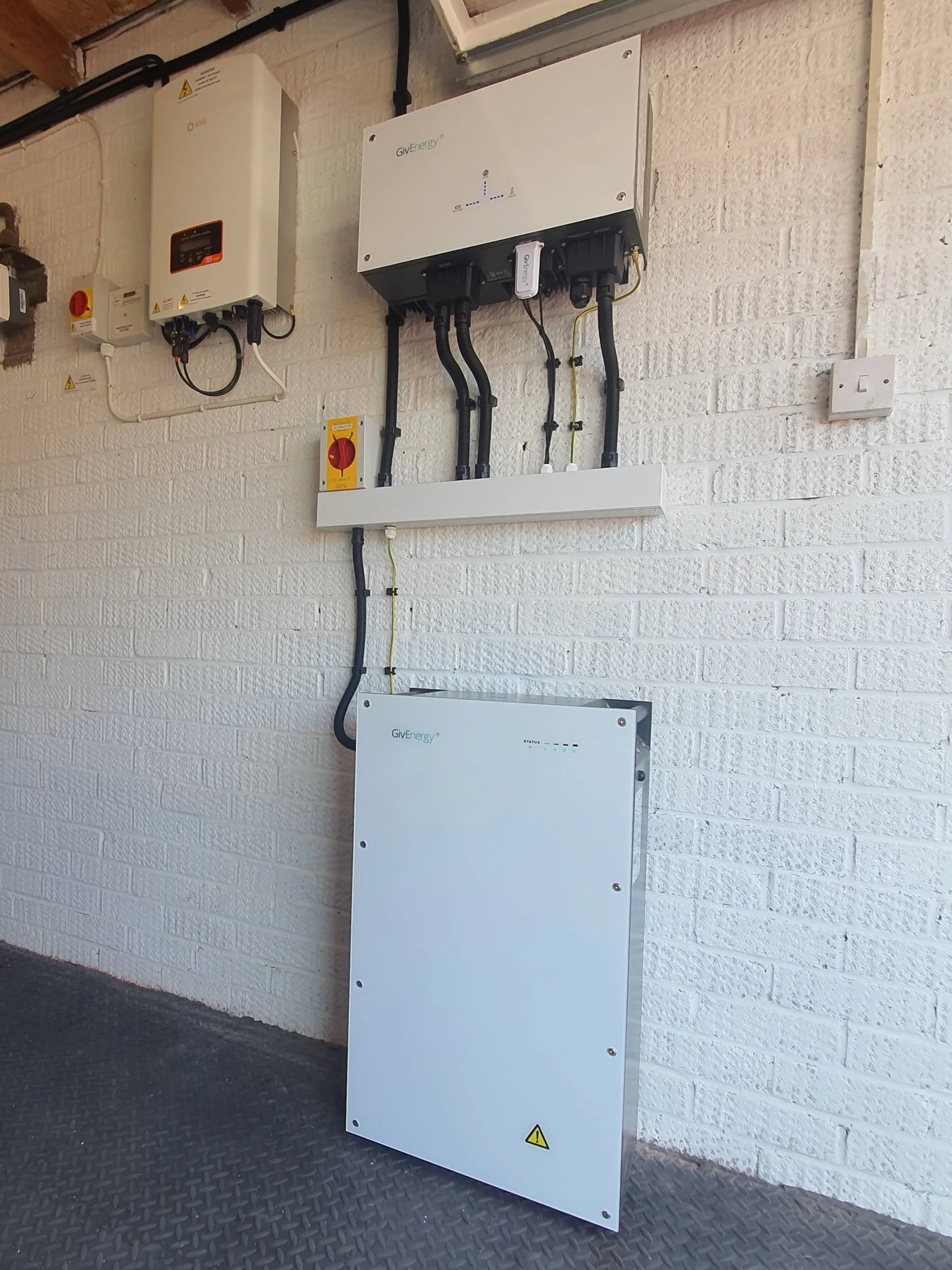 Solar power storage system with inverters and control panels on a white brick wall.