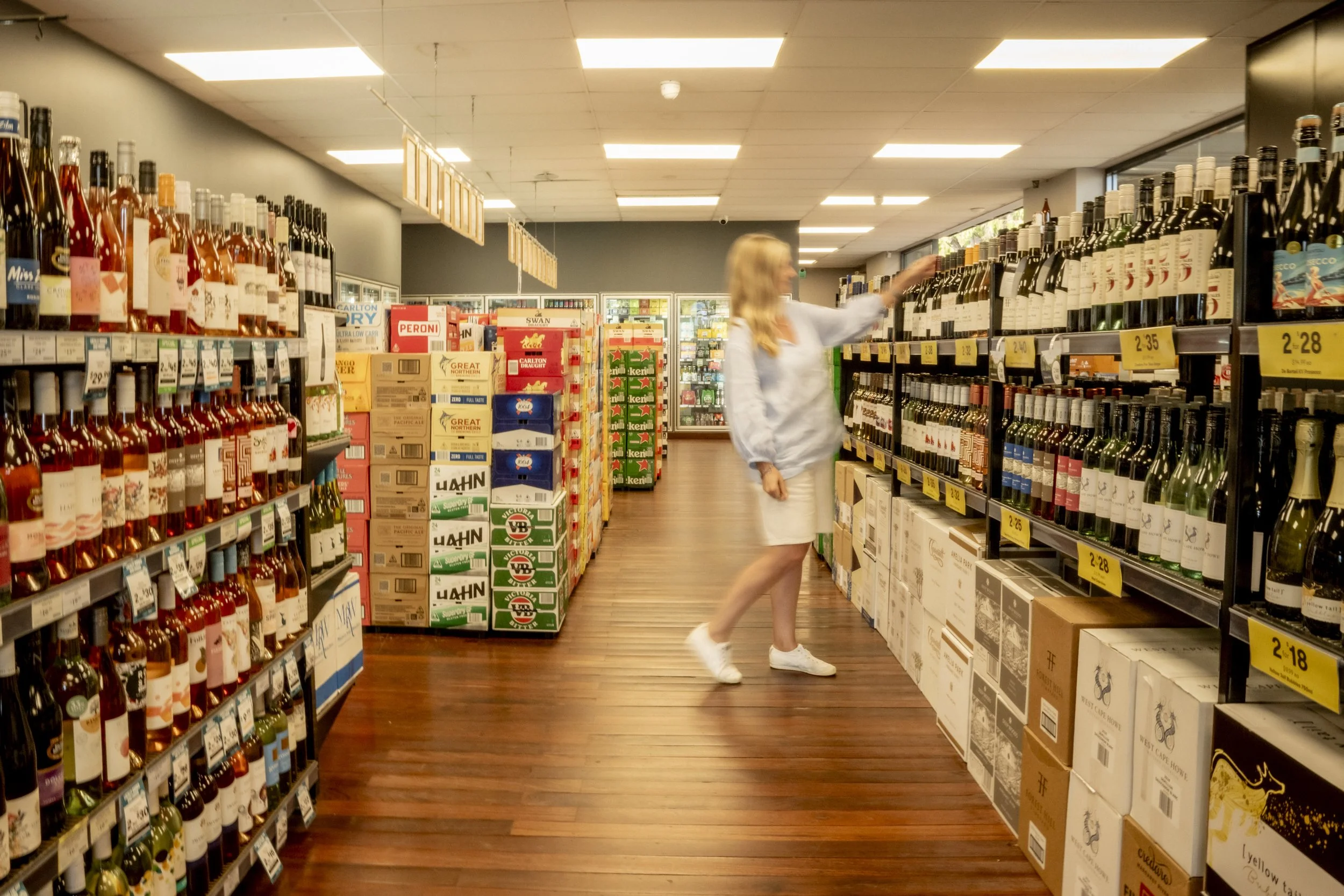 Customer browsing wine selection at Brew Plus bottle shop in Busselton, surrounded by boxed beer and local wines