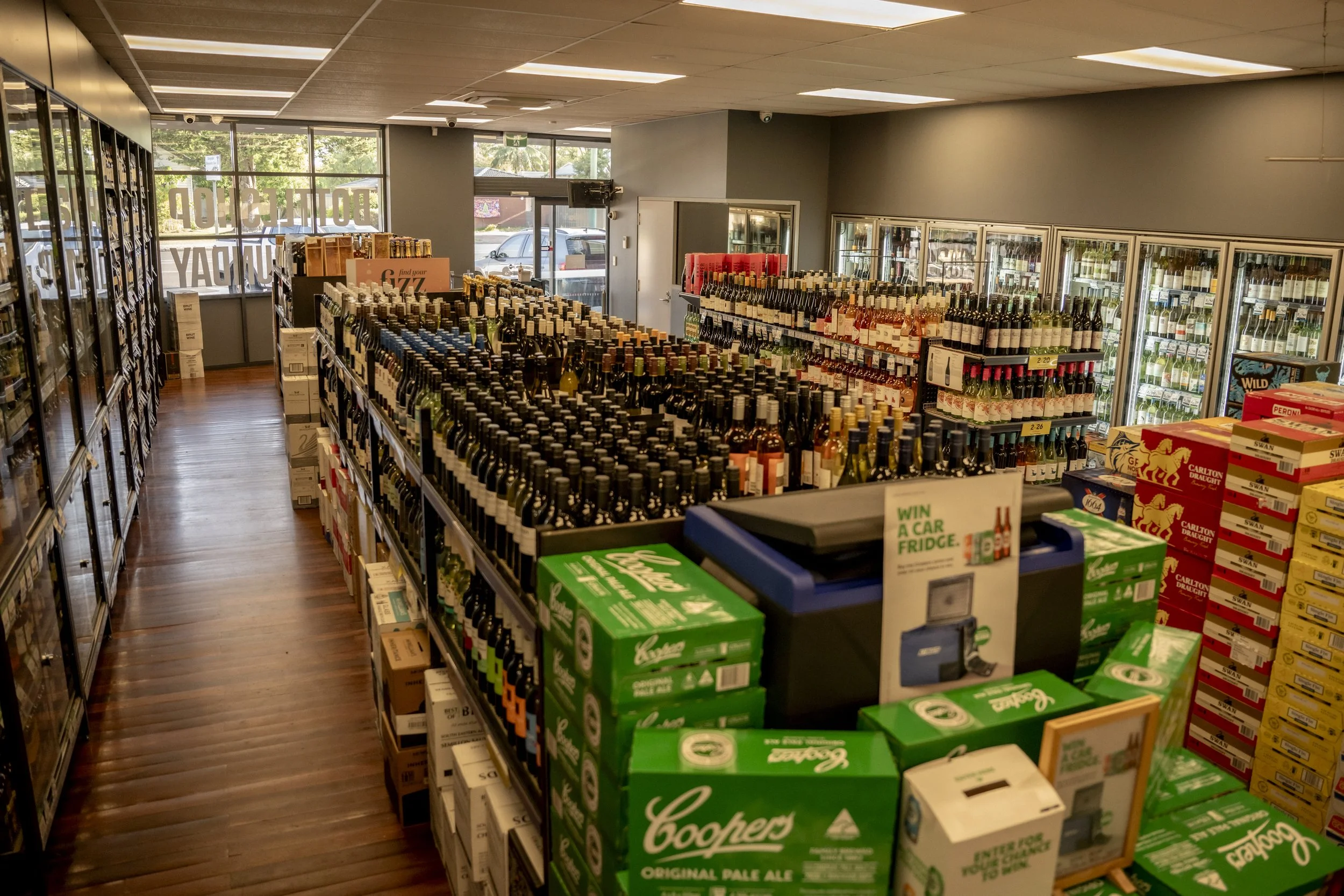 Wide selection of spirits and liquor bottles inside Brew Plus Busselton bottle shop, with chilled drinks and wine aisles visible