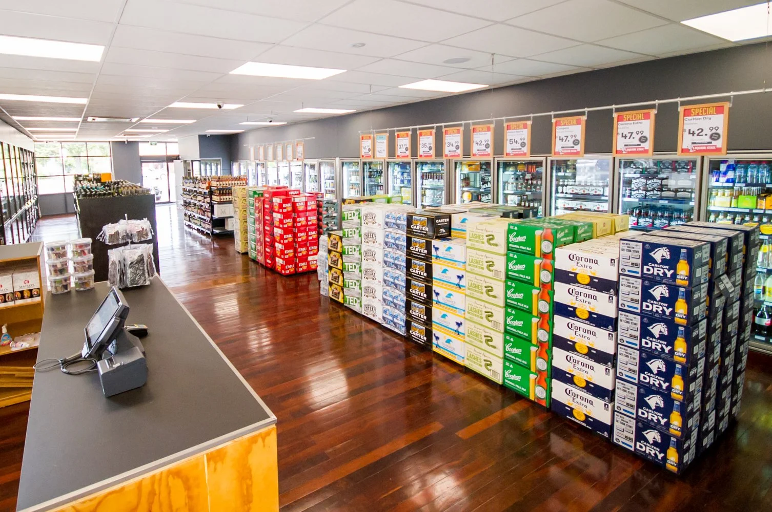 Interior of Brew Plus bottle shop in Busselton featuring stacked beer cartons, chilled drinks, and weekly specials