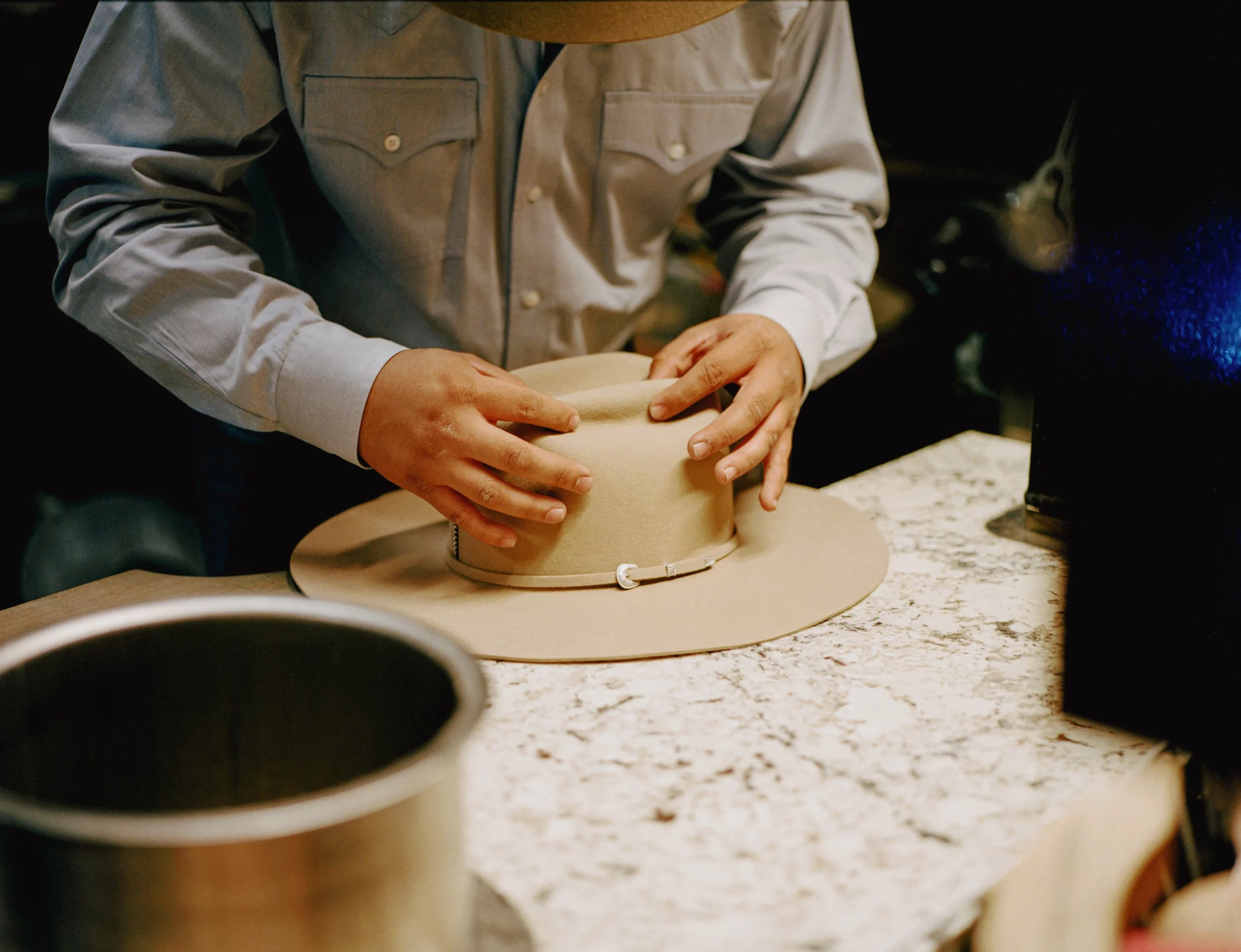 Person shaping a hat on a worktable in a dimly lit room.