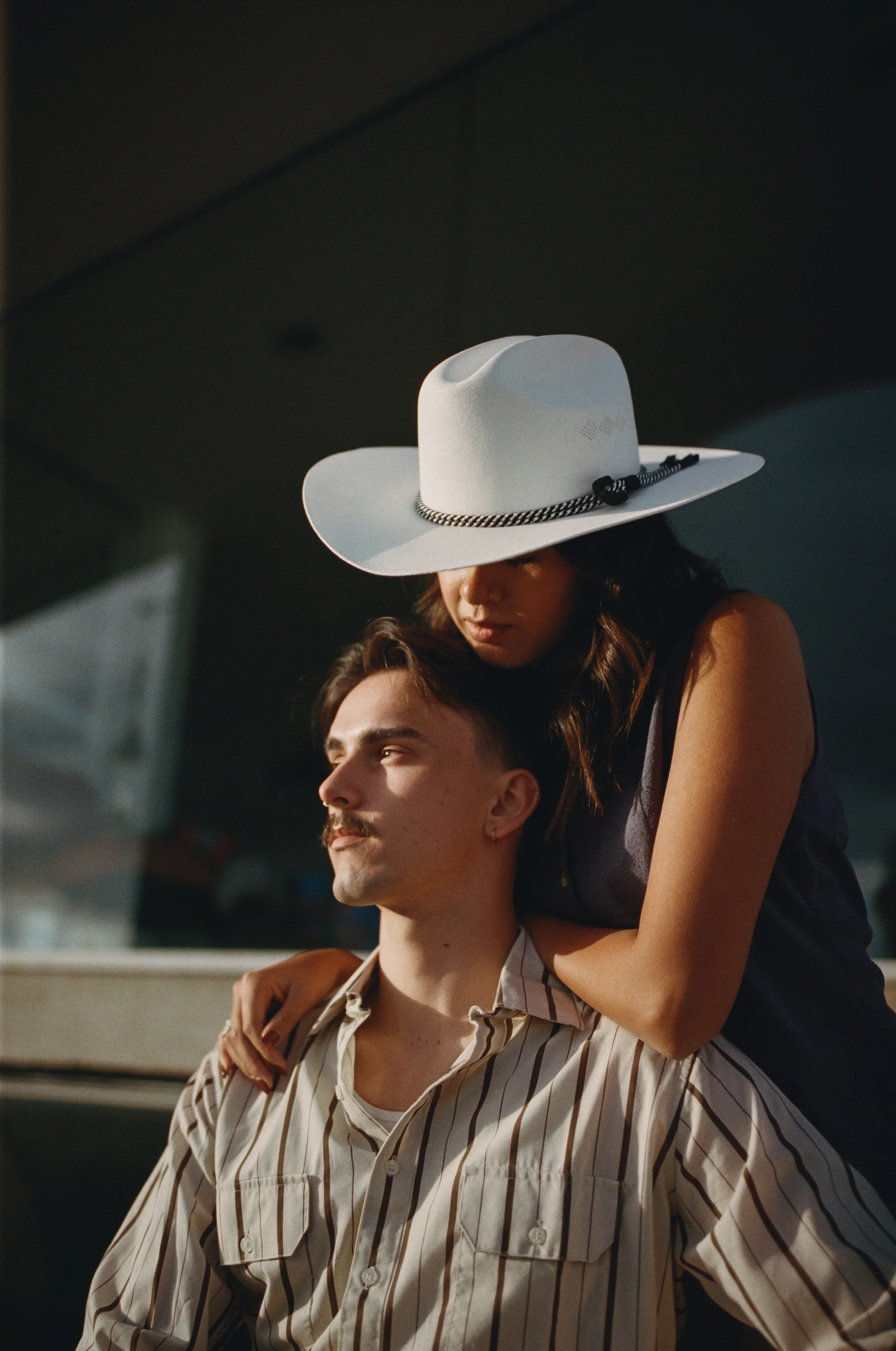 A woman with a white hat leaning over a man with a striped shirt, both sitting close together.
