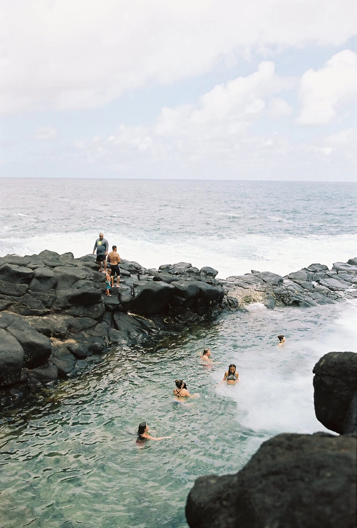 People swimming in a rocky ocean cove under a cloudy sky.