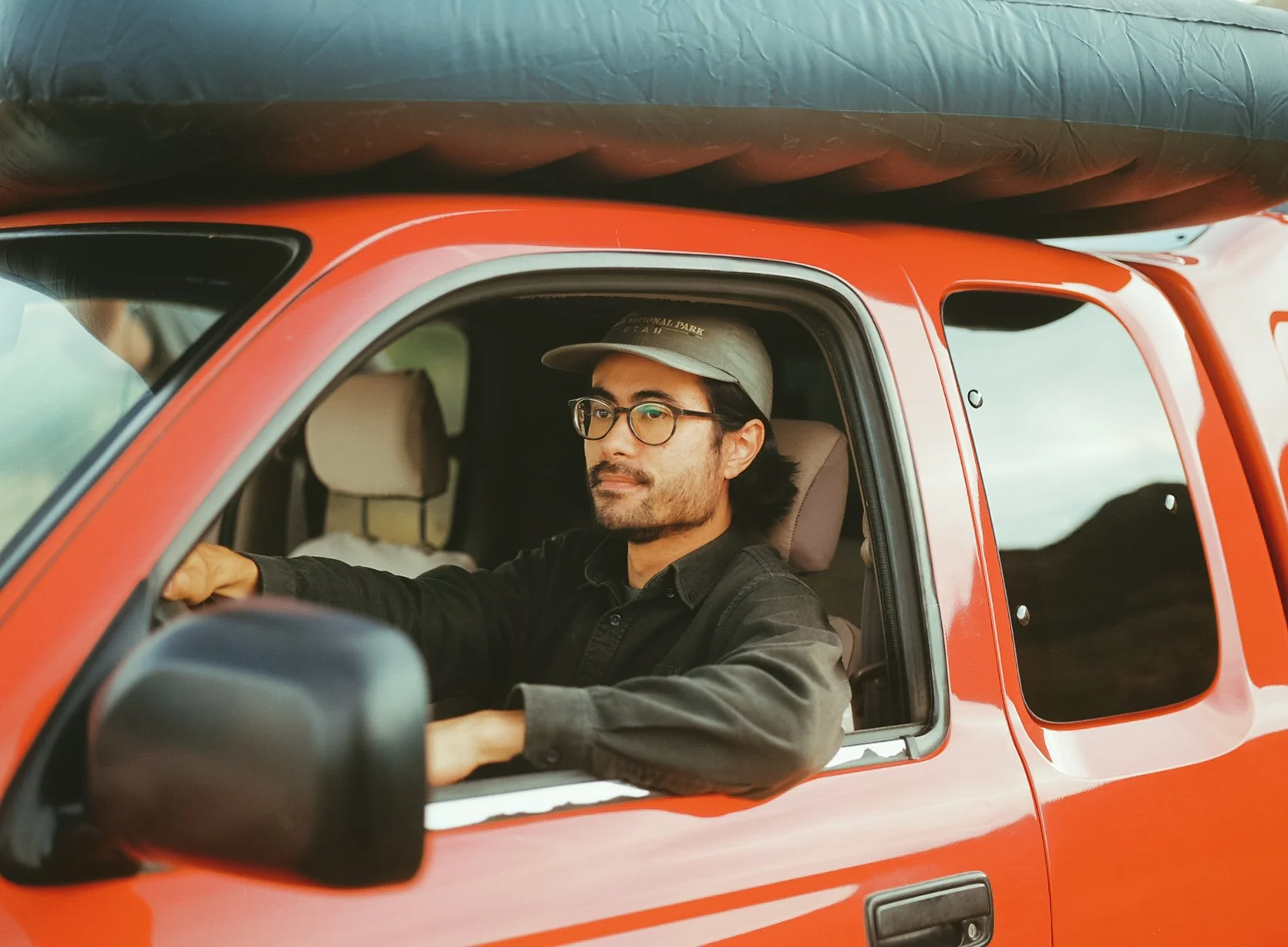 Man with glasses and a cap driving a red vehicle during daytime