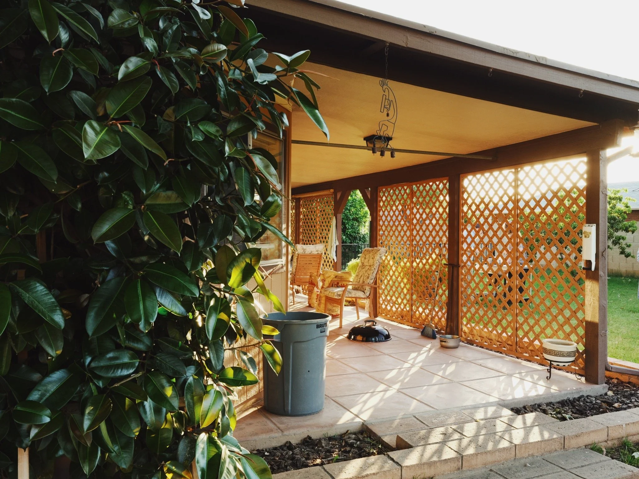 Back porch with wooden lattice panels, chairs, a robotic vacuum, a trash can, and outdoor plants.