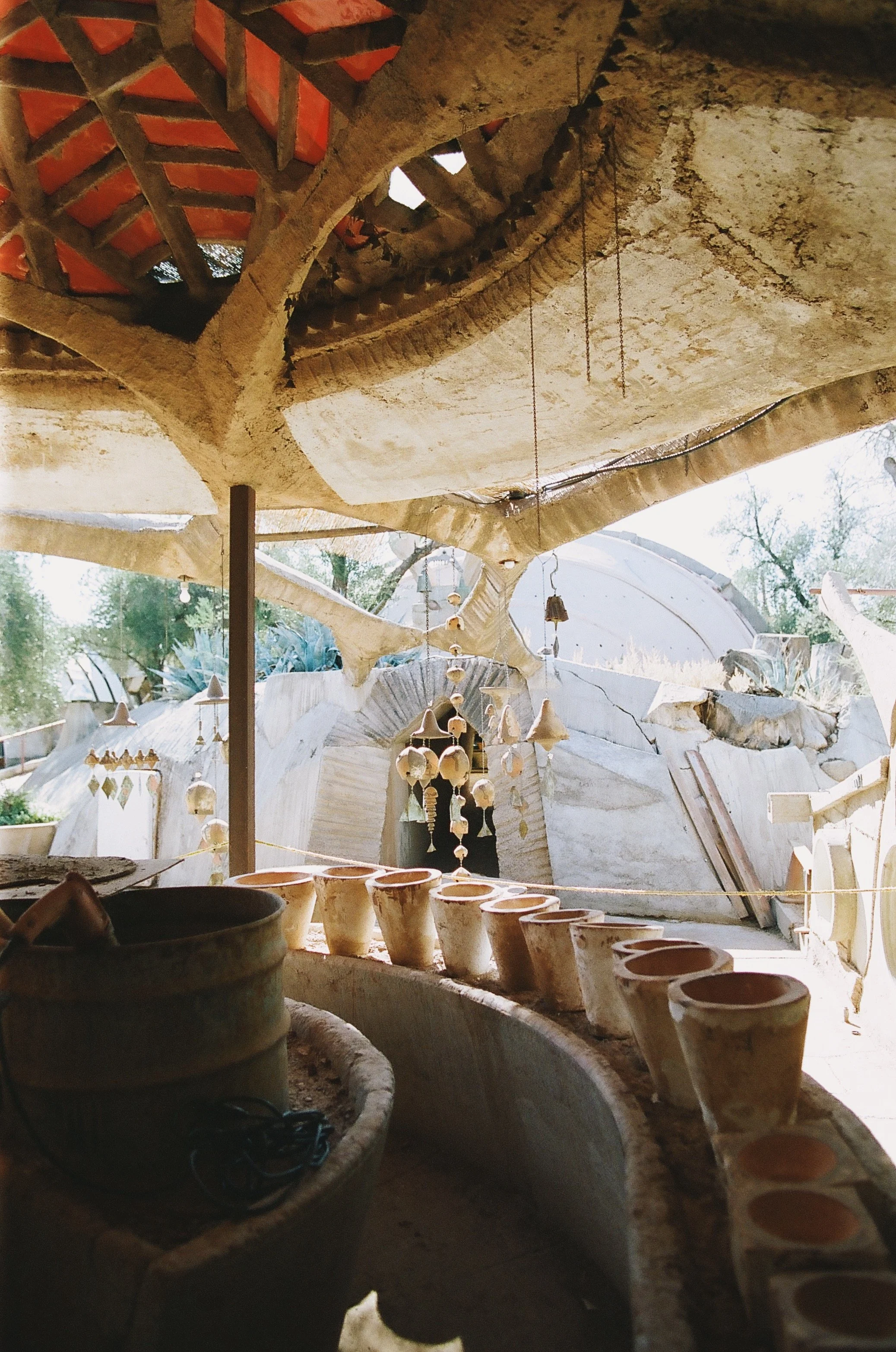 Clay pots arranged in a row on a curved surface inside a pottery studio with hanging shells and natural light.