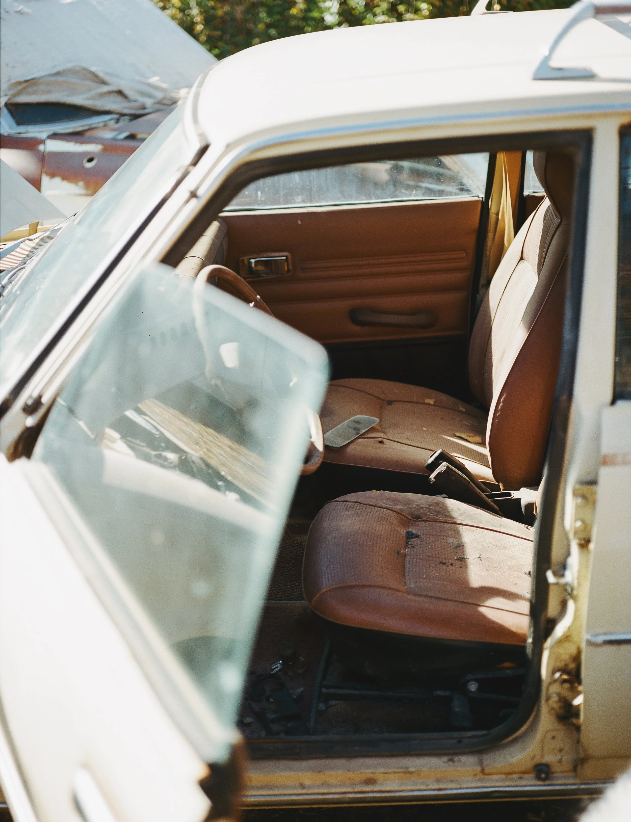Inside an old, abandoned car with brown seats and a dusty interior, parked outdoors on a sunny day.