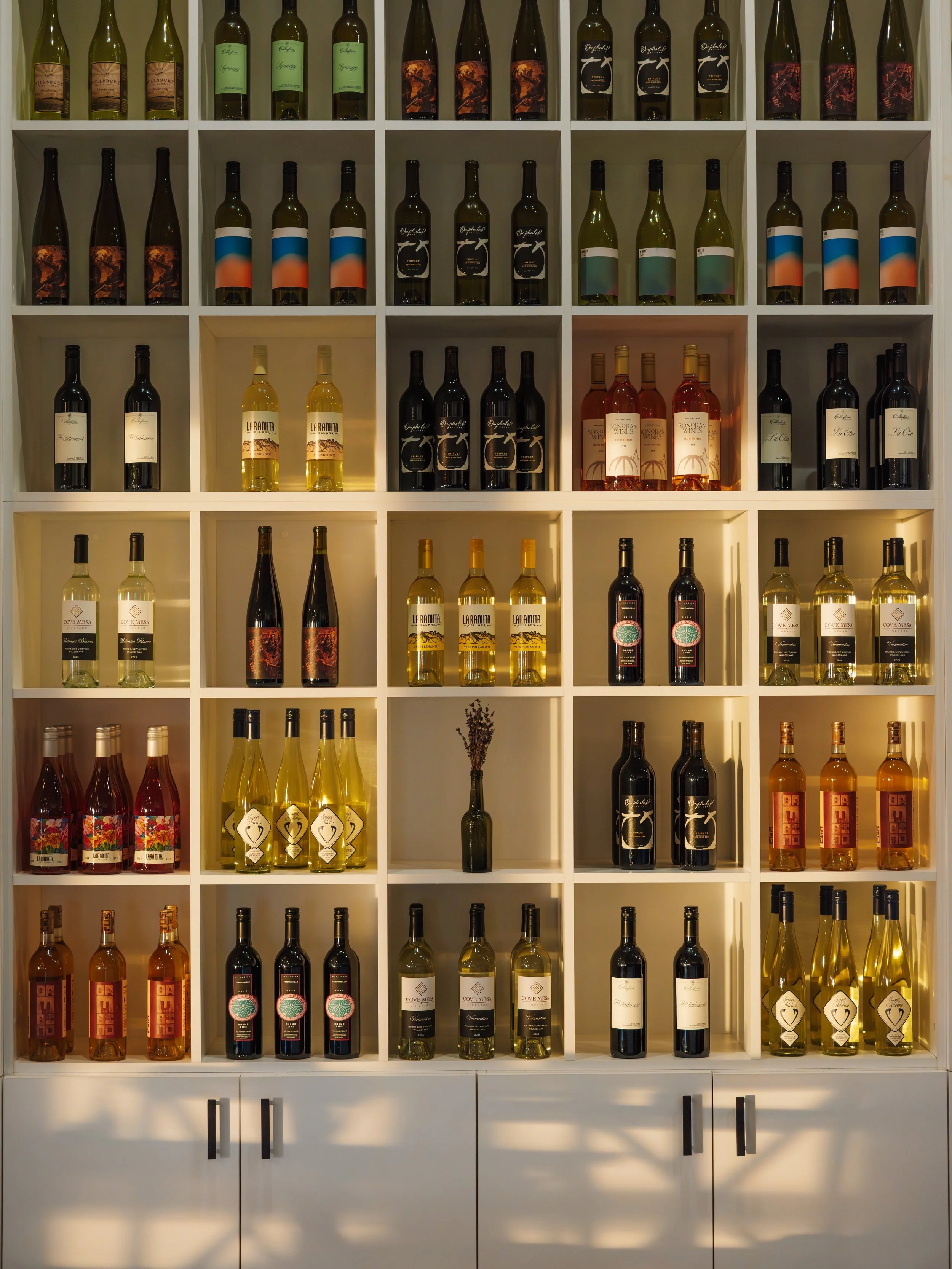 A white shelf filled with various bottles of wine organized by type and color.