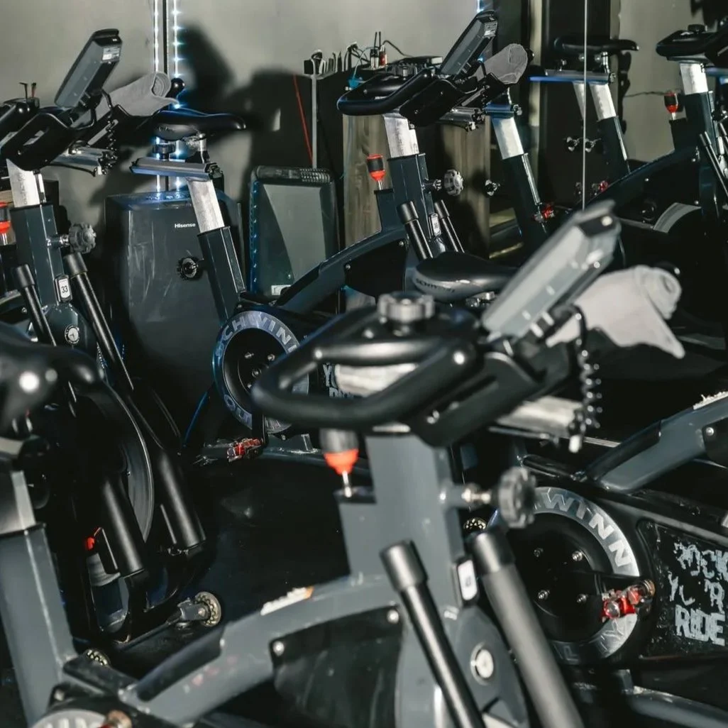 Several stationary exercise bikes arranged indoors in a dimly lit room.