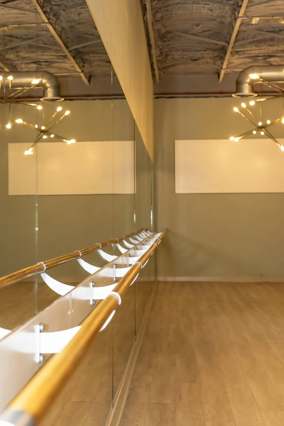Dance studio with mirrored wall, wooden ballet barre, and ceiling lighting fixtures.