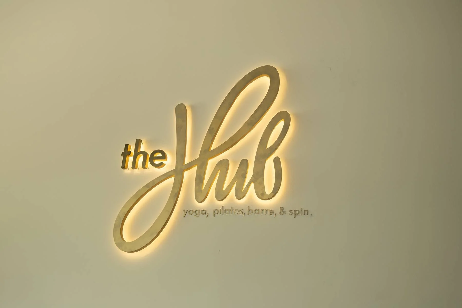 Neon sign on a white wall reads 'the self' in large cursive letters with 'the' in small lowercase letters, and below it in smaller font, 'yoga, pilates, barre, & spin.'