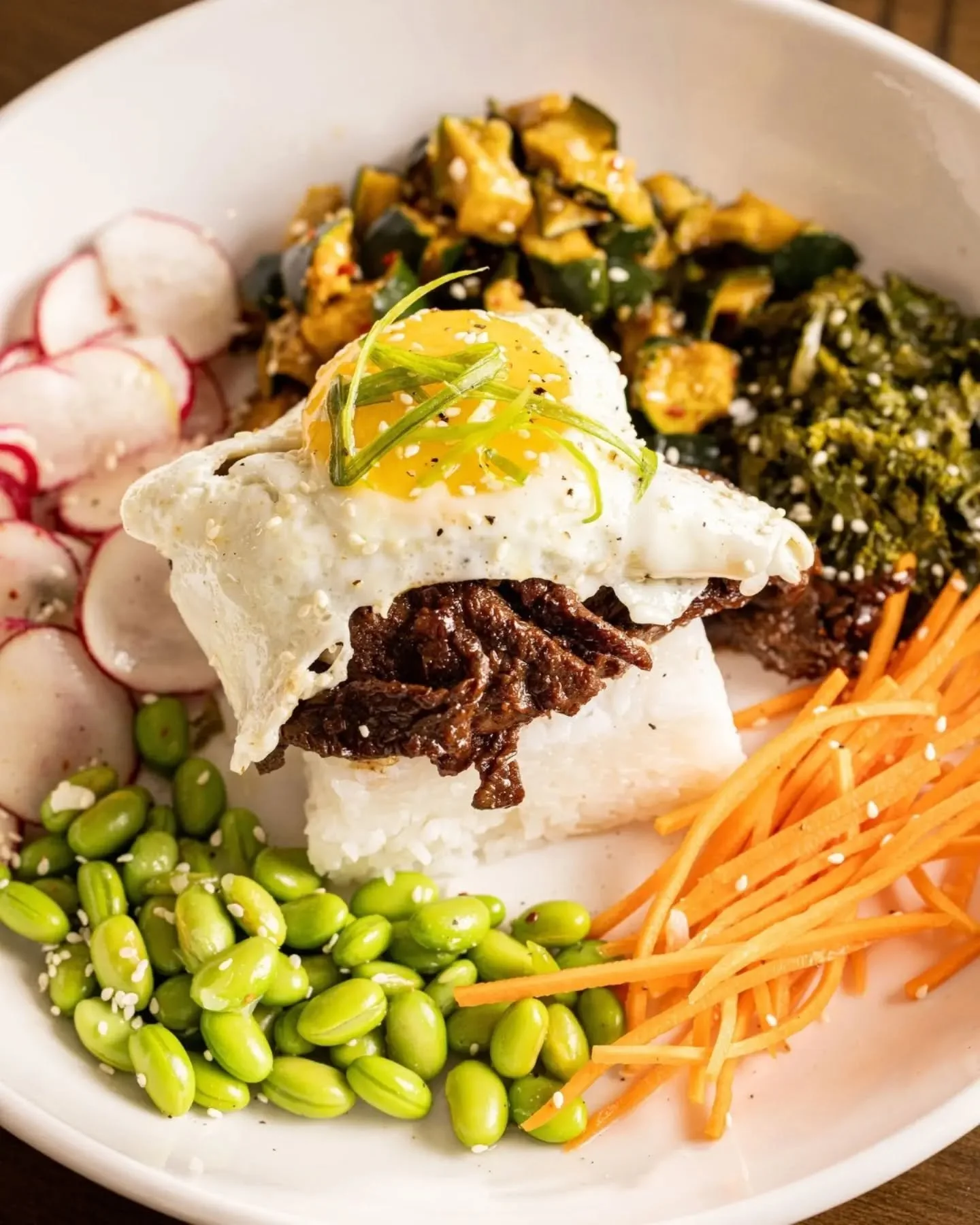 Your lunch plans just got better. 🥢 Our Sesame Steak Bowl is loaded with sesame soy&ndash;marinated sirloin, pickled kale, edamame, julienne carrots, marinated cucumbers, green onions, a crispy rice cake, and a fried egg on top.

Fresh, flavorful, a