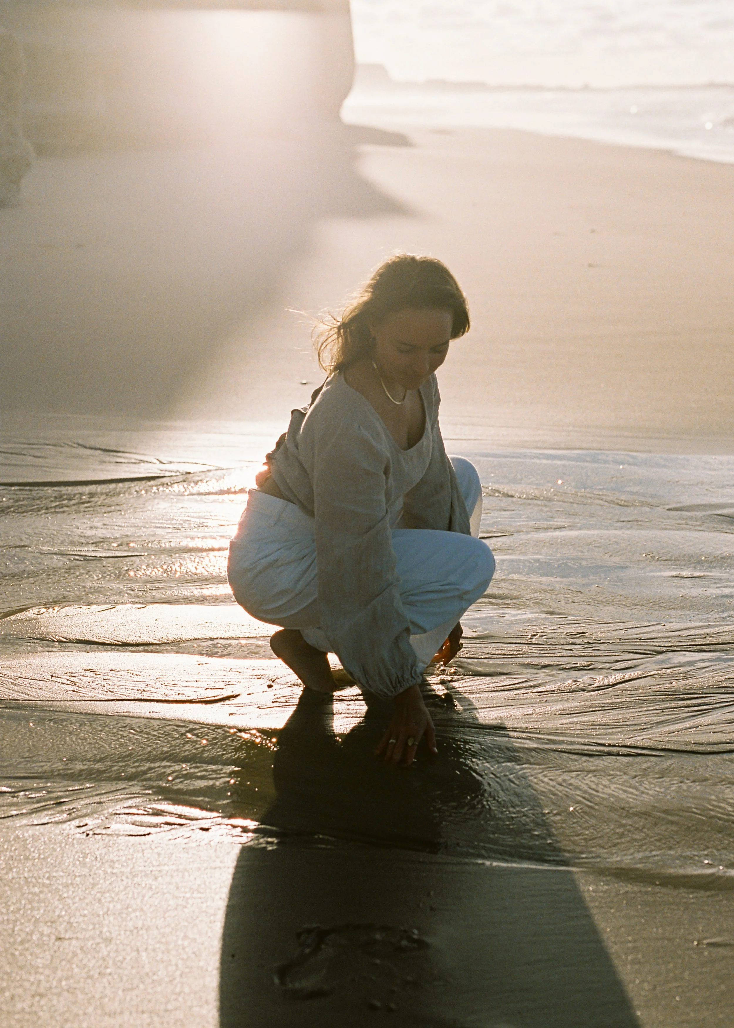 Annabel kneeling on a beach, connecting with the water