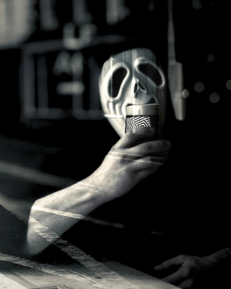 Black and white image of a man in a spooky mask holding a beer.