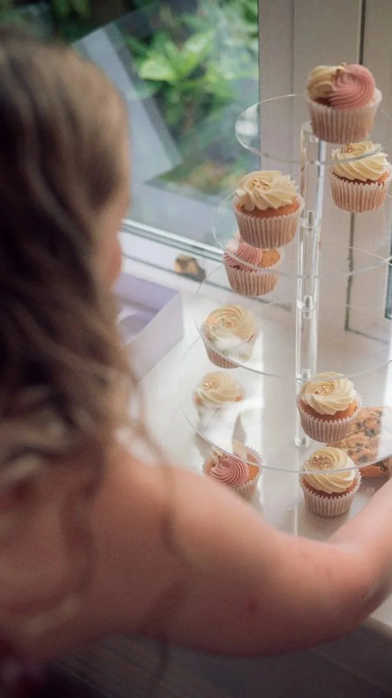 A person looking at a display of decorated cupcakes on a tiered stand near a window.