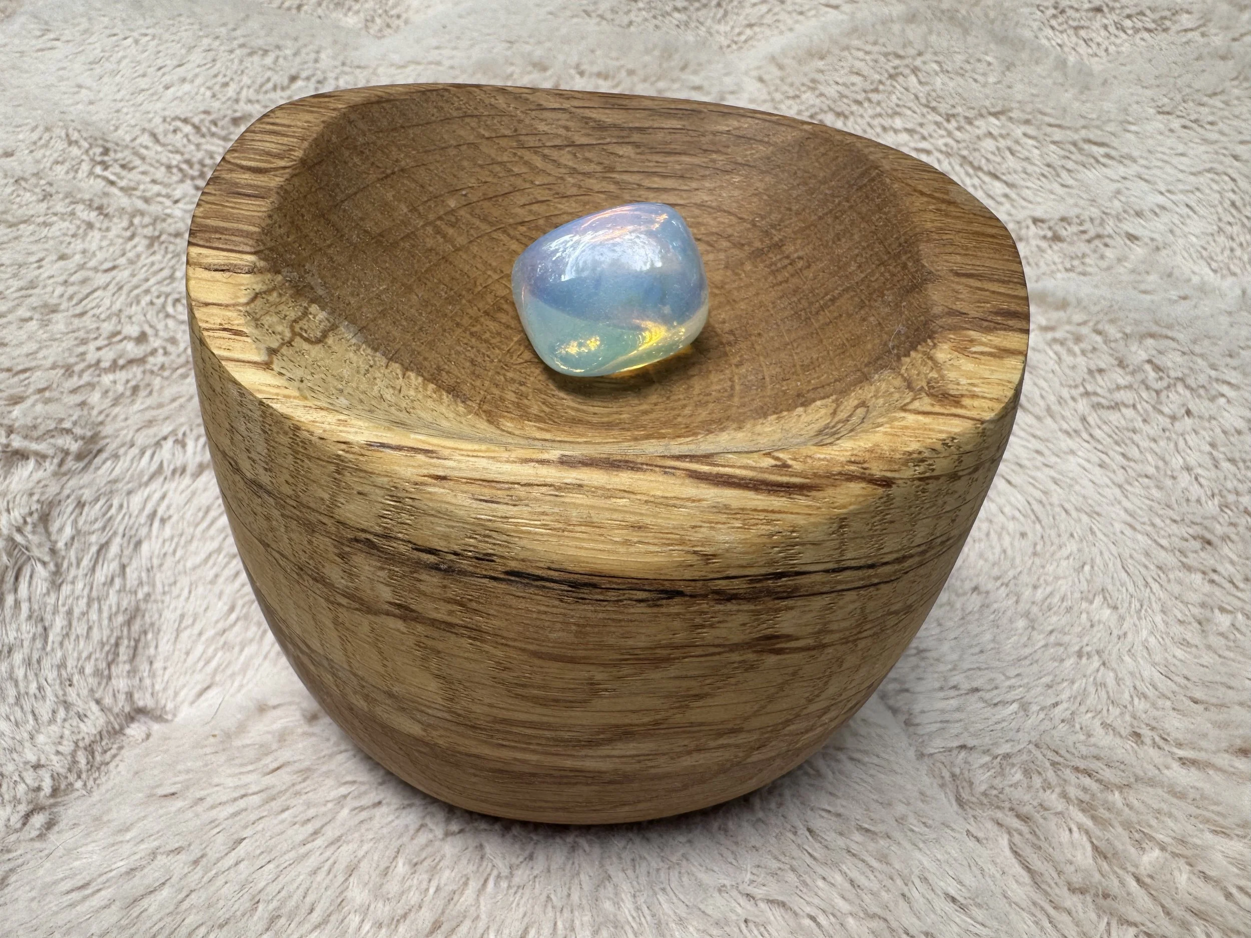 Single opalite stone resting in a hand-carved wooden bowl by Tamara Albright on a soft, warm beige textured background, accompanying the Direction stage of Allvibe Creative’s Brand Design process.
