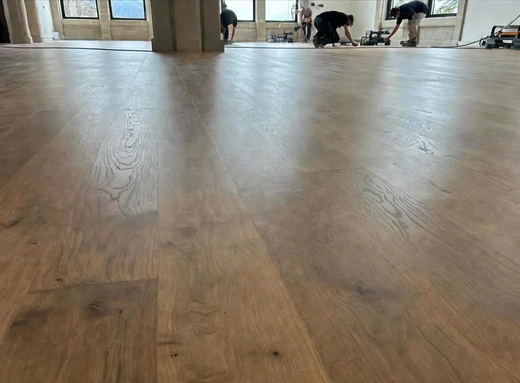 photo of a new hardwood floor with workers in the background nailing the floor