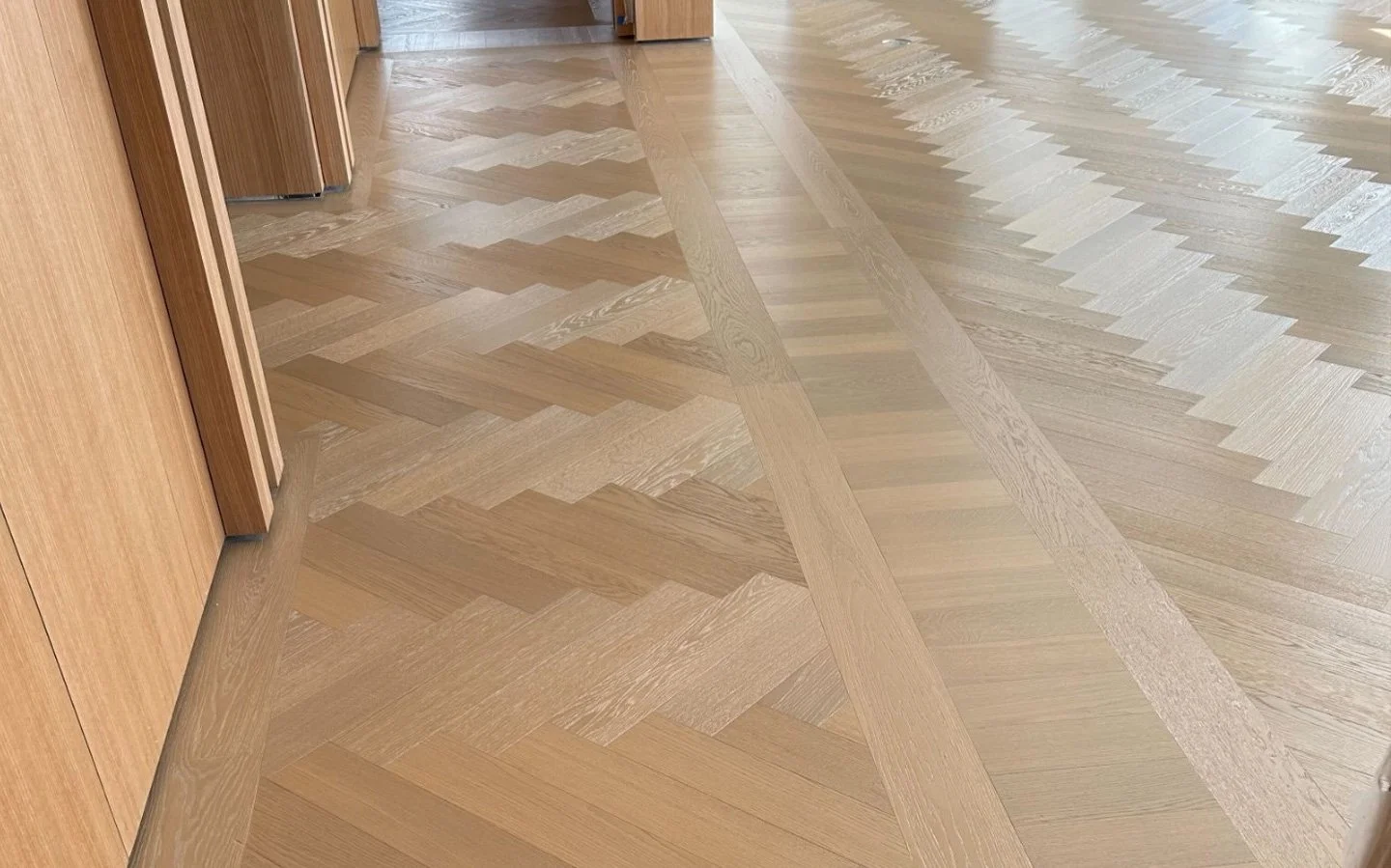 Light oak herringbone parquet hardwood flooring with a chevron border design in a modern interior.