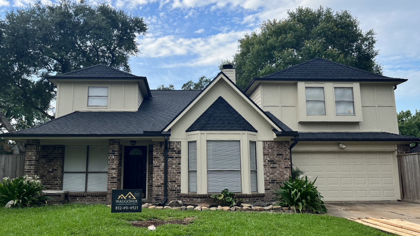 Front view of a two-story house with brick and white siding, black roof, and attached garage, with green lawn and trees in background.