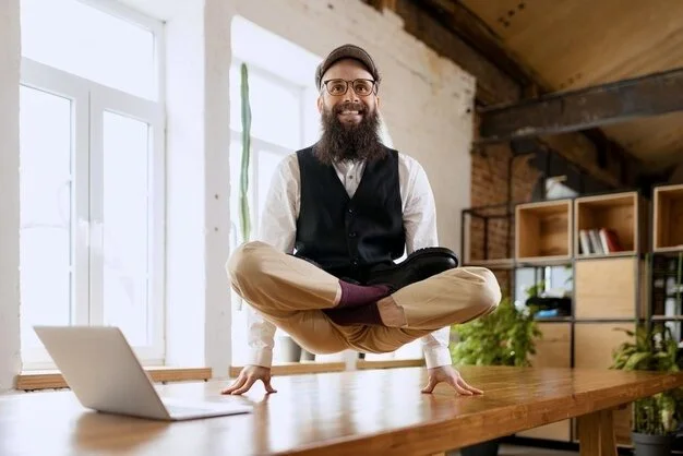 man doing the lotus yoga position on his finger tips on top of a desk in the office