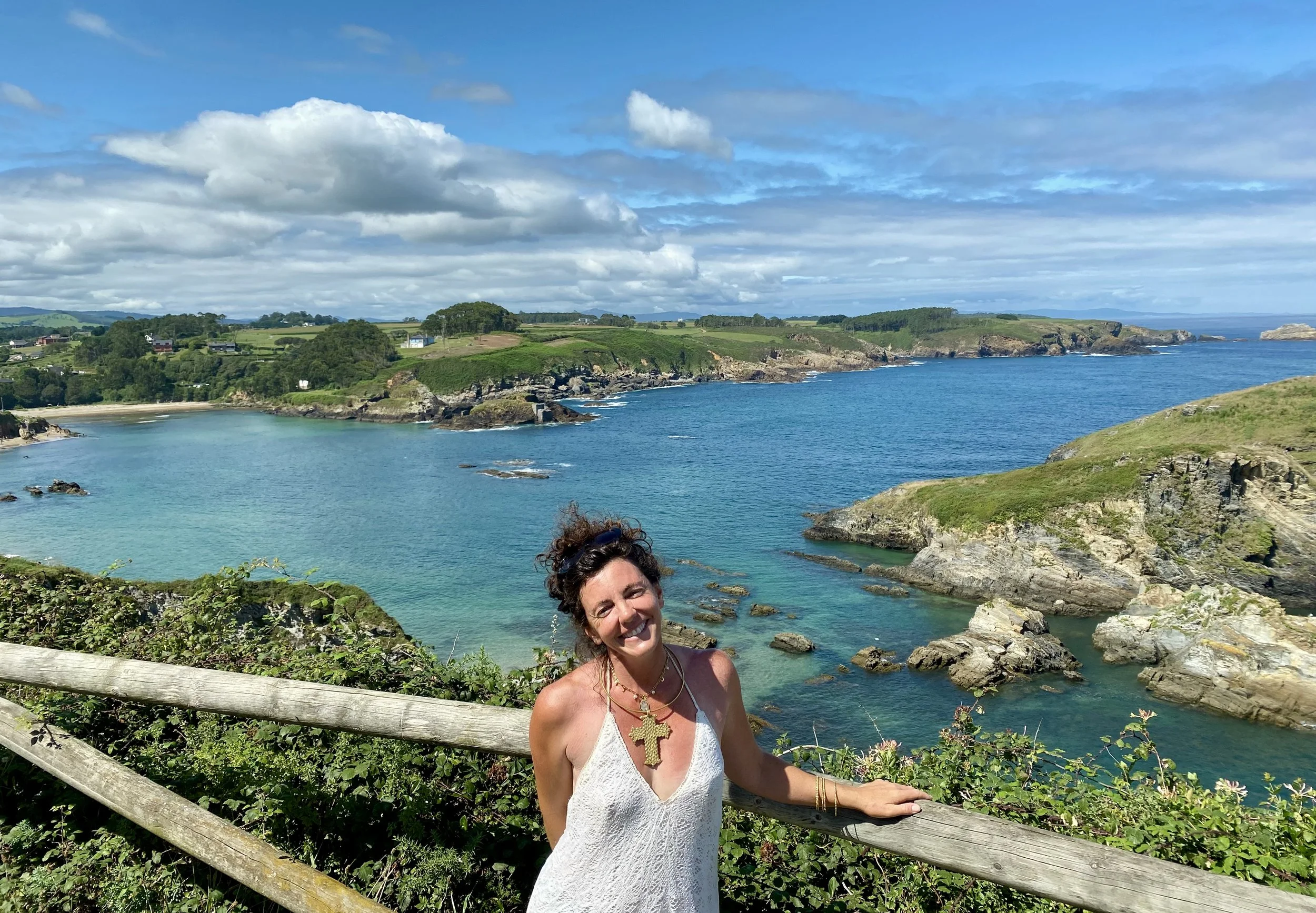 Woman in white dress smiling stood by ocean backdrop
