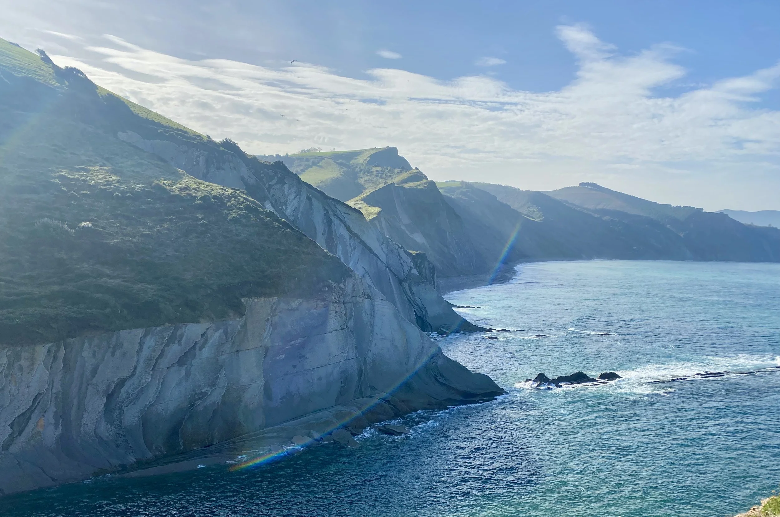 Beautiful cliffs into the ocean, with blue sunny sky and rolling green hills in background