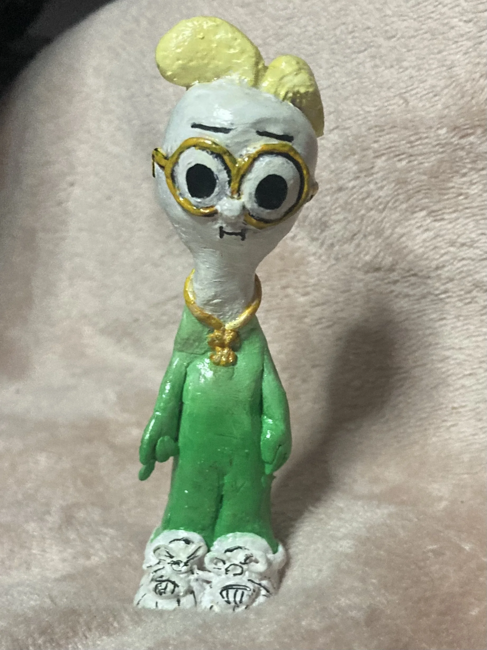 Handcrafted figurine of a person with large glasses, green clothing, and white shoes, standing on a textured white base.