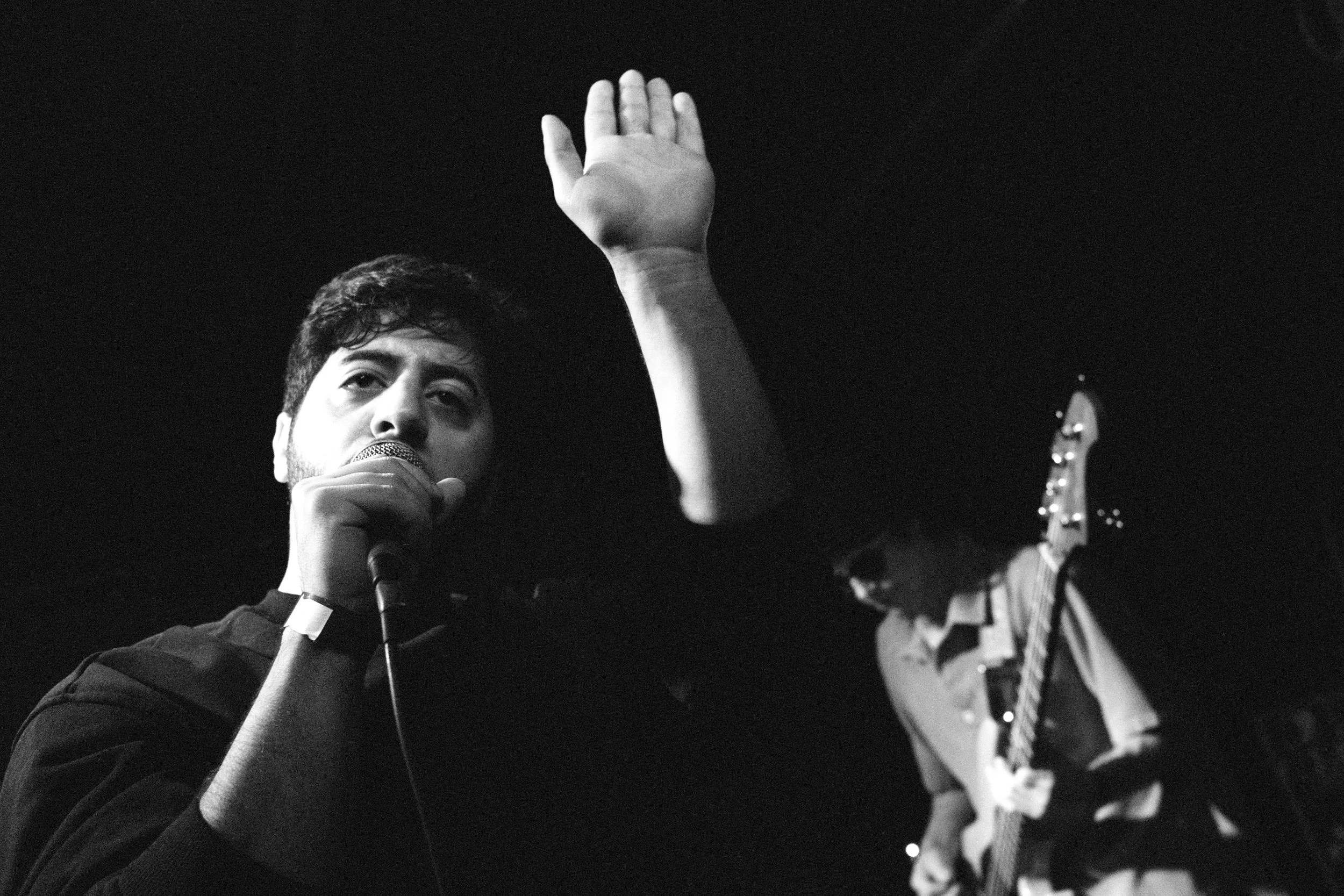 Black-and-white photo of Prostitute’s vocalist performing live at Le Chinois in Paris, arm raised above the crowd while the bassist plays behind them during the Attempted Martyr set.