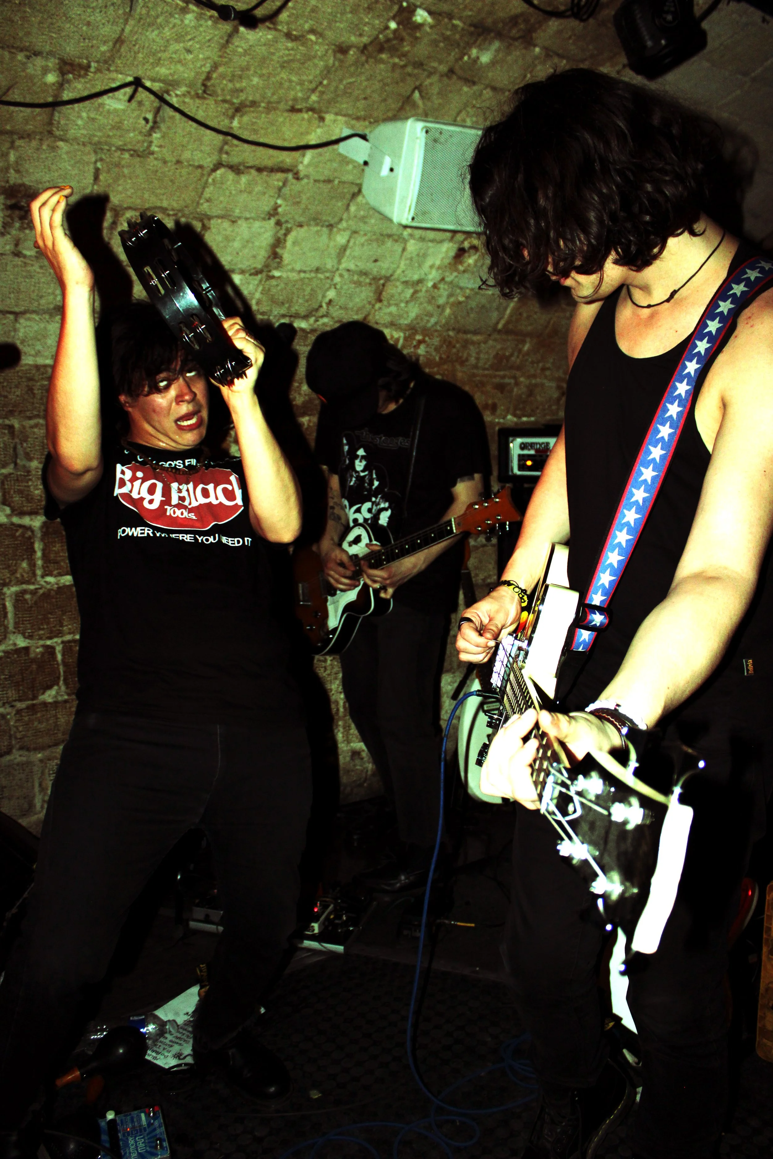 Winona Riders live onstage, captured by Noize Mag in a cramped brick-walled venue, delivering the relentless psychedelic battery of Winona Riders with a frenzied tambourine-wielding vocalist and sweat-soaked guitarist mid-performance.