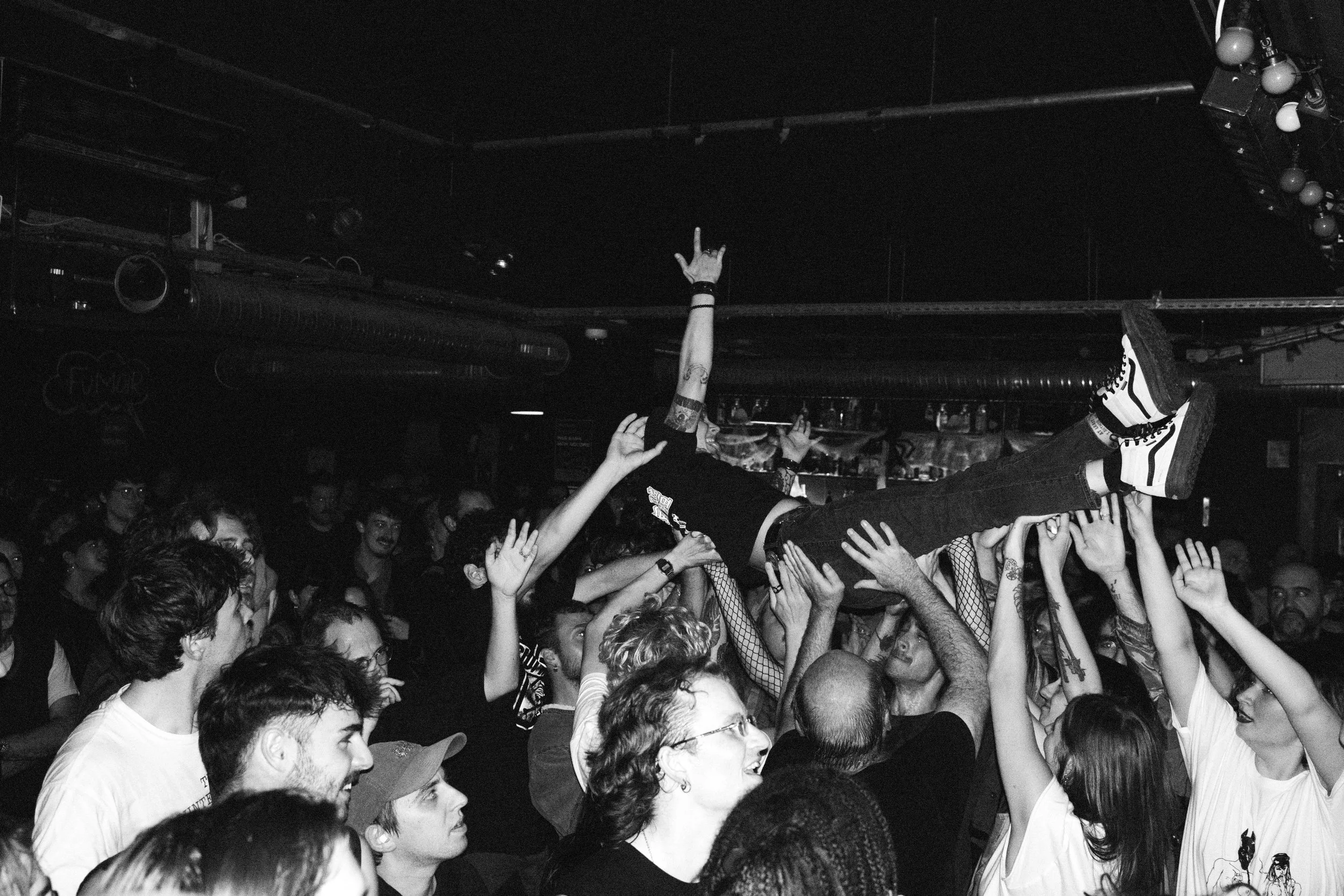 High-energy black-and-white shot of a fan crowd-surfing during Prostitute’s Paris show at Le Chinois, with a packed noise-punk audience lifting them above the floor.