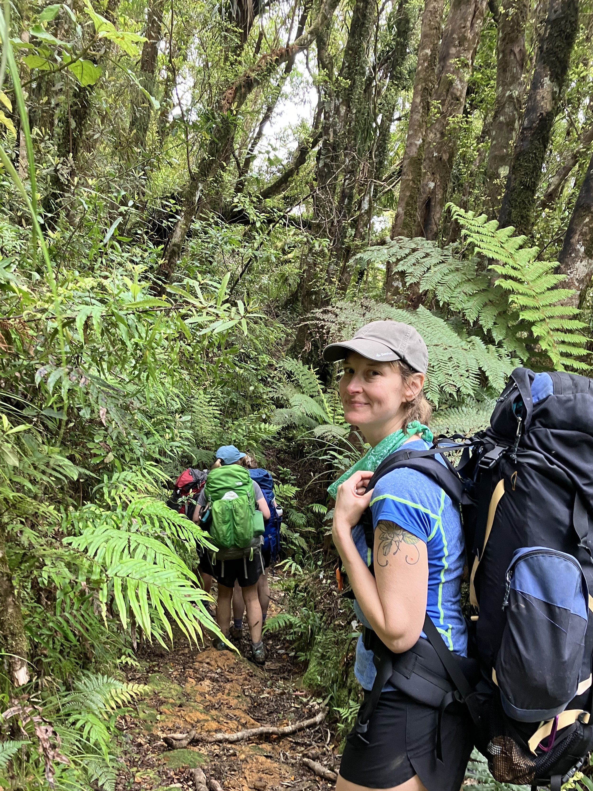 A woman in a grey hat is hiking and smiling at the camera