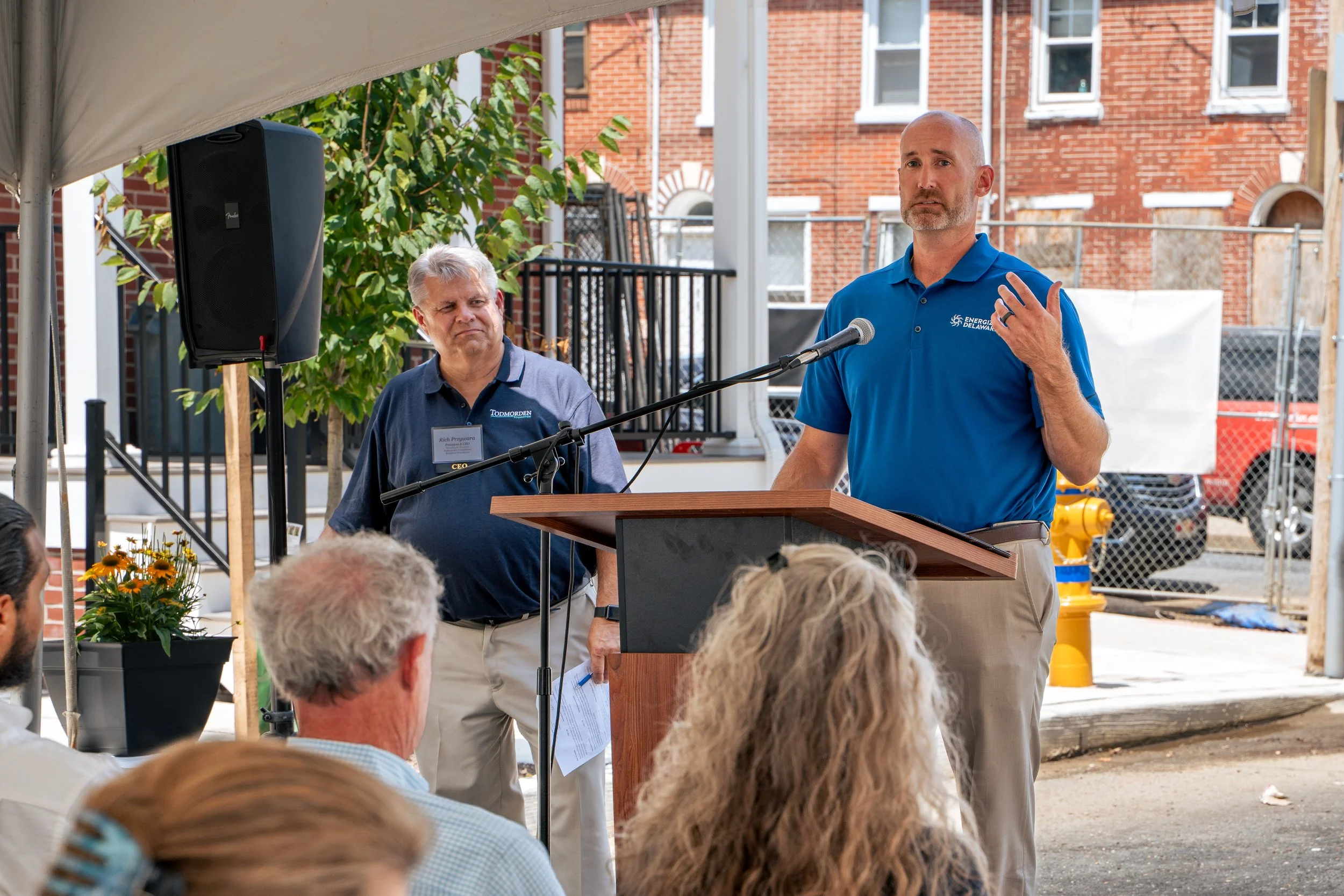 A man in a blue shirt is giving a speech at a podium