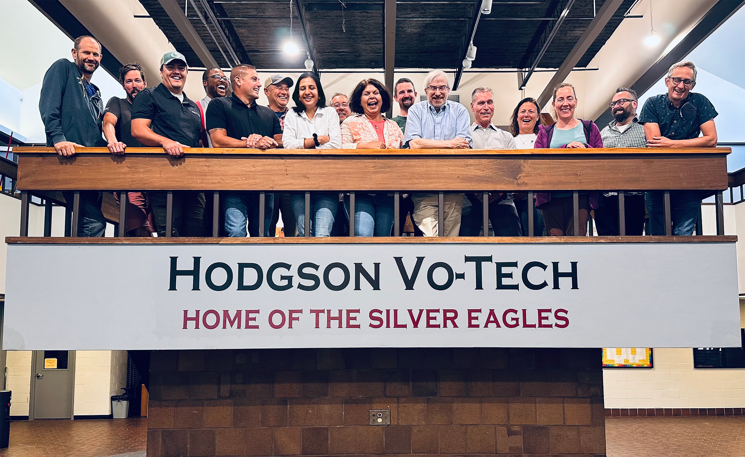A group of people stand on an elevated platform over a sign that says "Hodgson Vo-Tech, Home of the Silver Eagles"